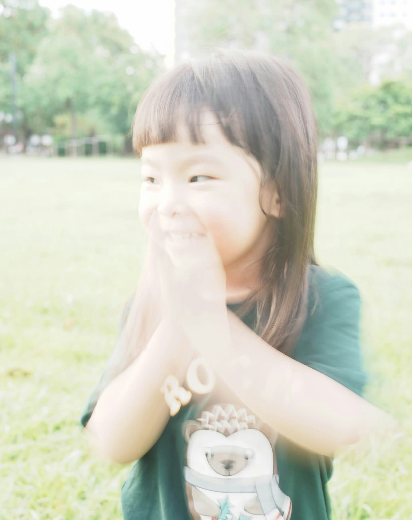 公園で手を口元に当てる子どもの笑顔