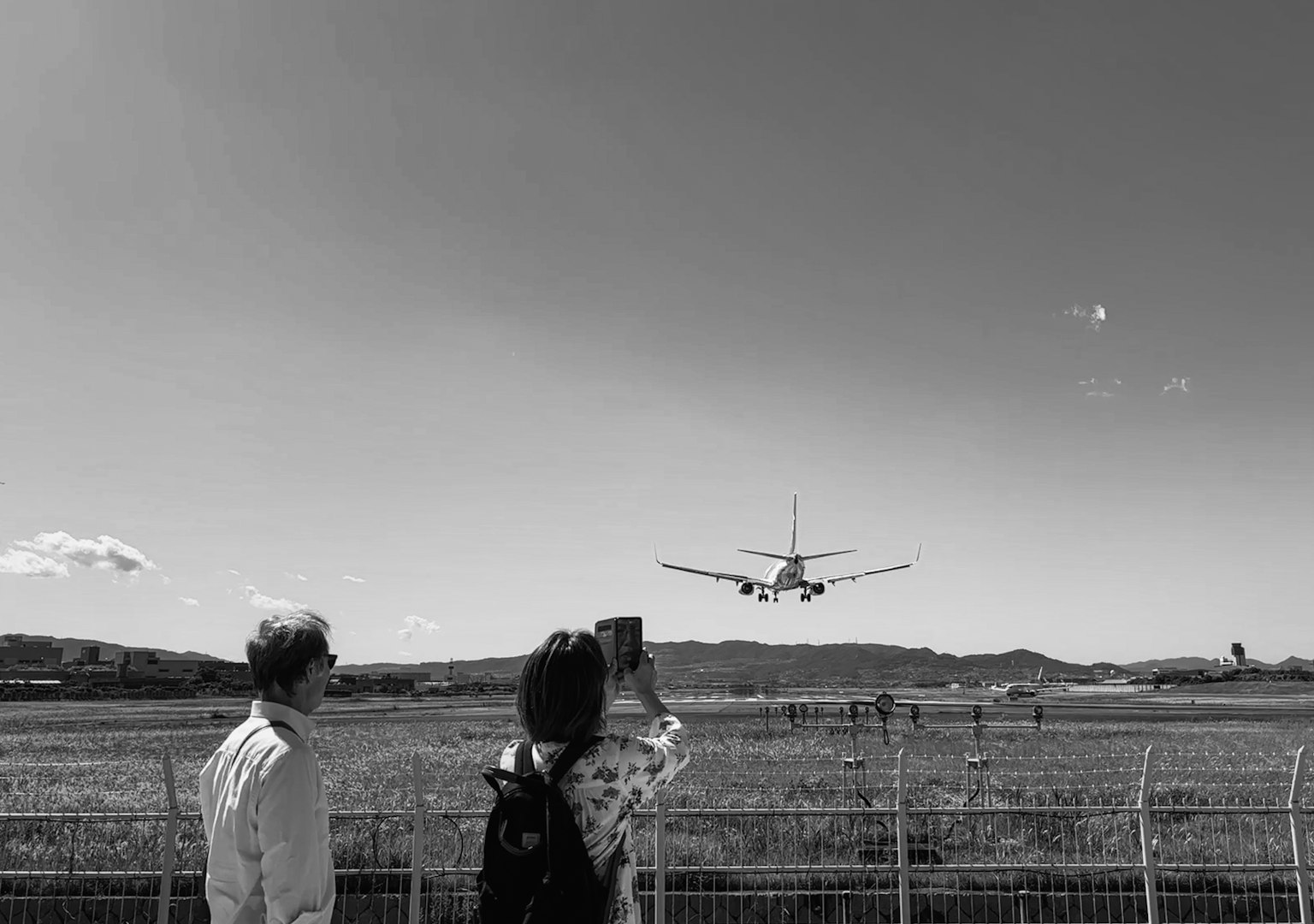Due turisti che guardano un aereo atterrare in un aeroporto
