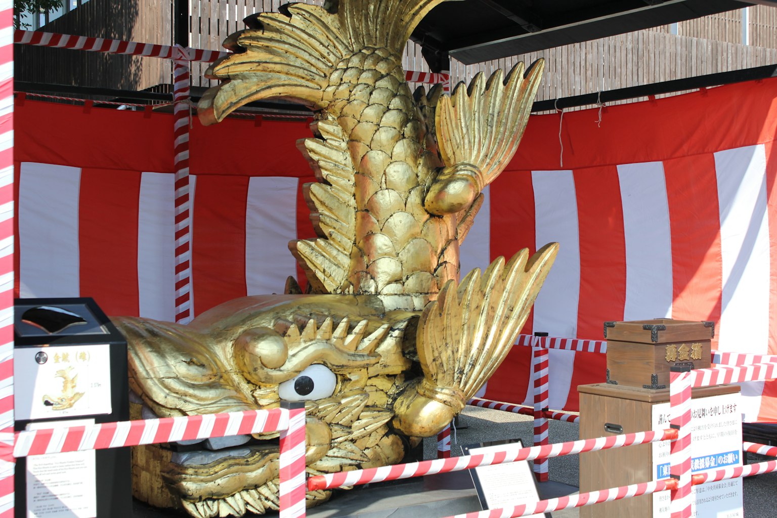Escultura de pez dorado dentro de un puesto con fondo de rayas rojas y blancas