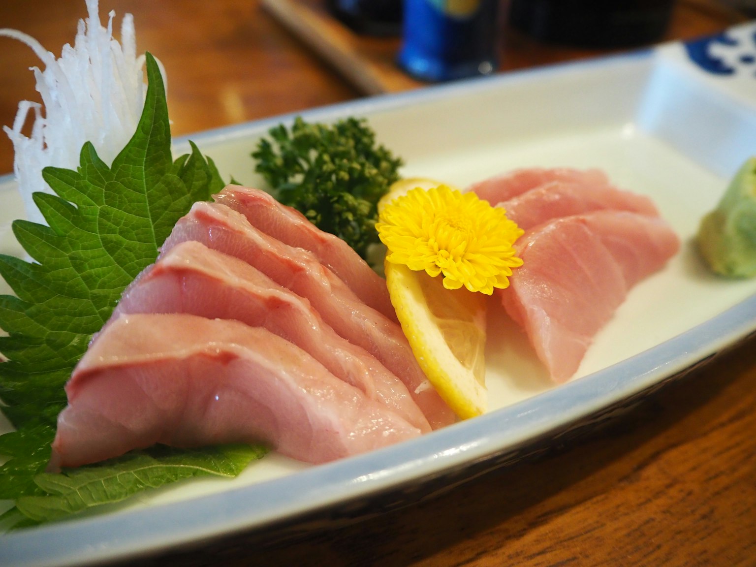 Fresh sashimi platter featuring tuna slices lemon wasabi and green leaves