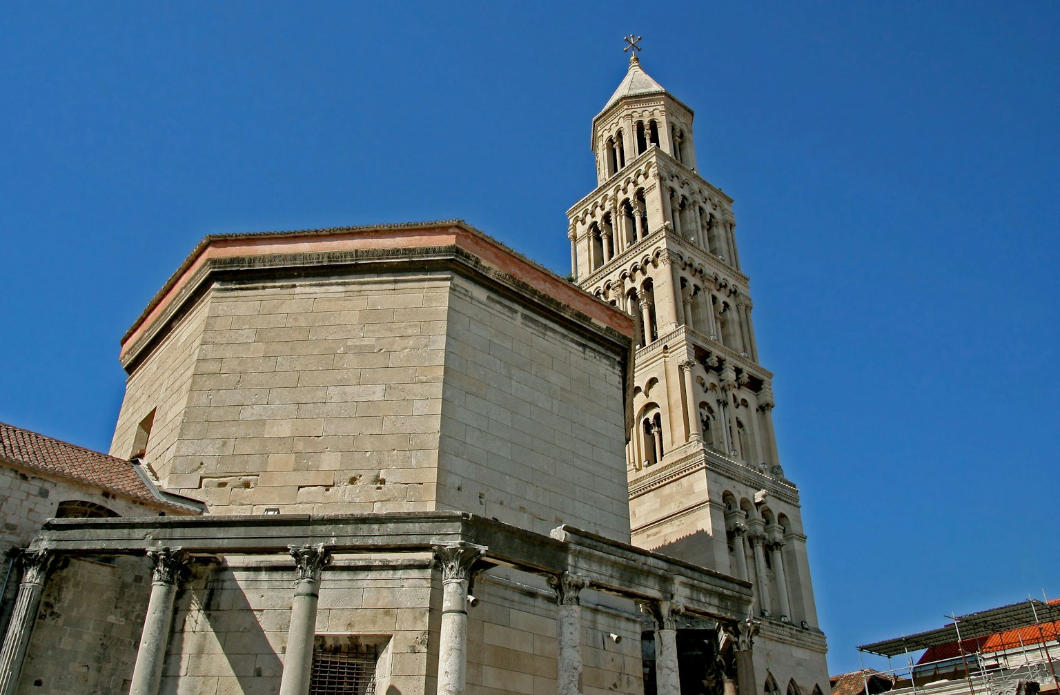 Vista della torre campanaria del Palazzo di Diocleziano e di un edificio in pietra sotto un cielo azzurro