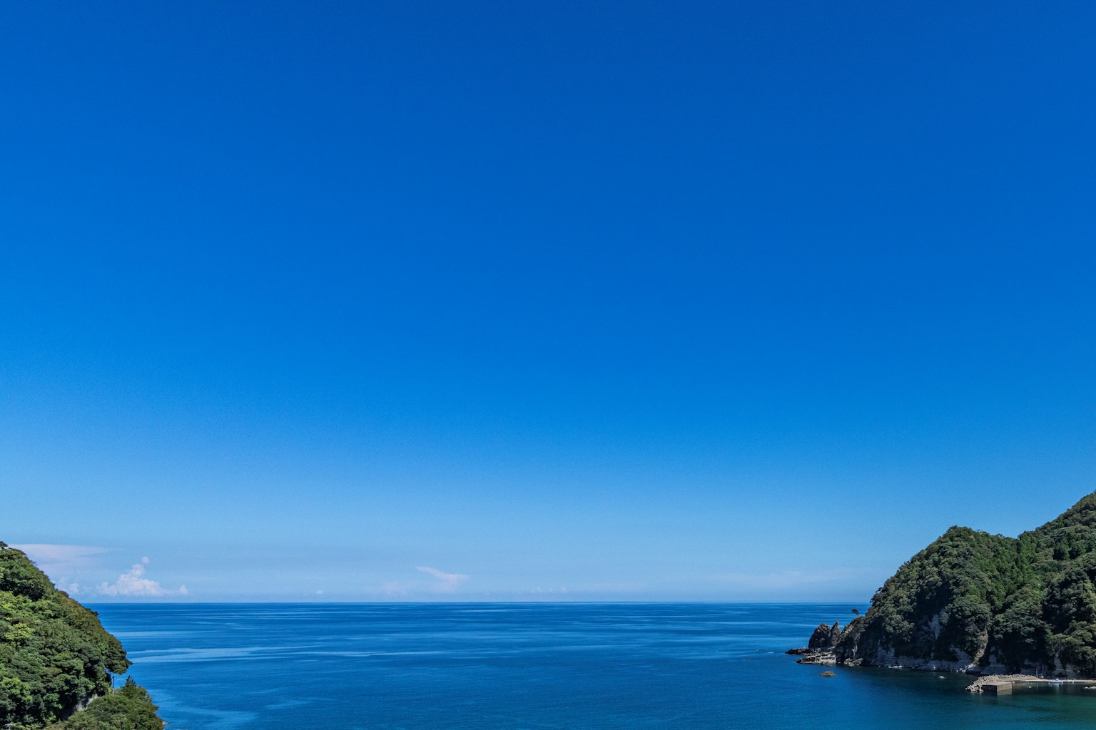 Scena di cielo blu vibrante e oceano circondato da colline verdi