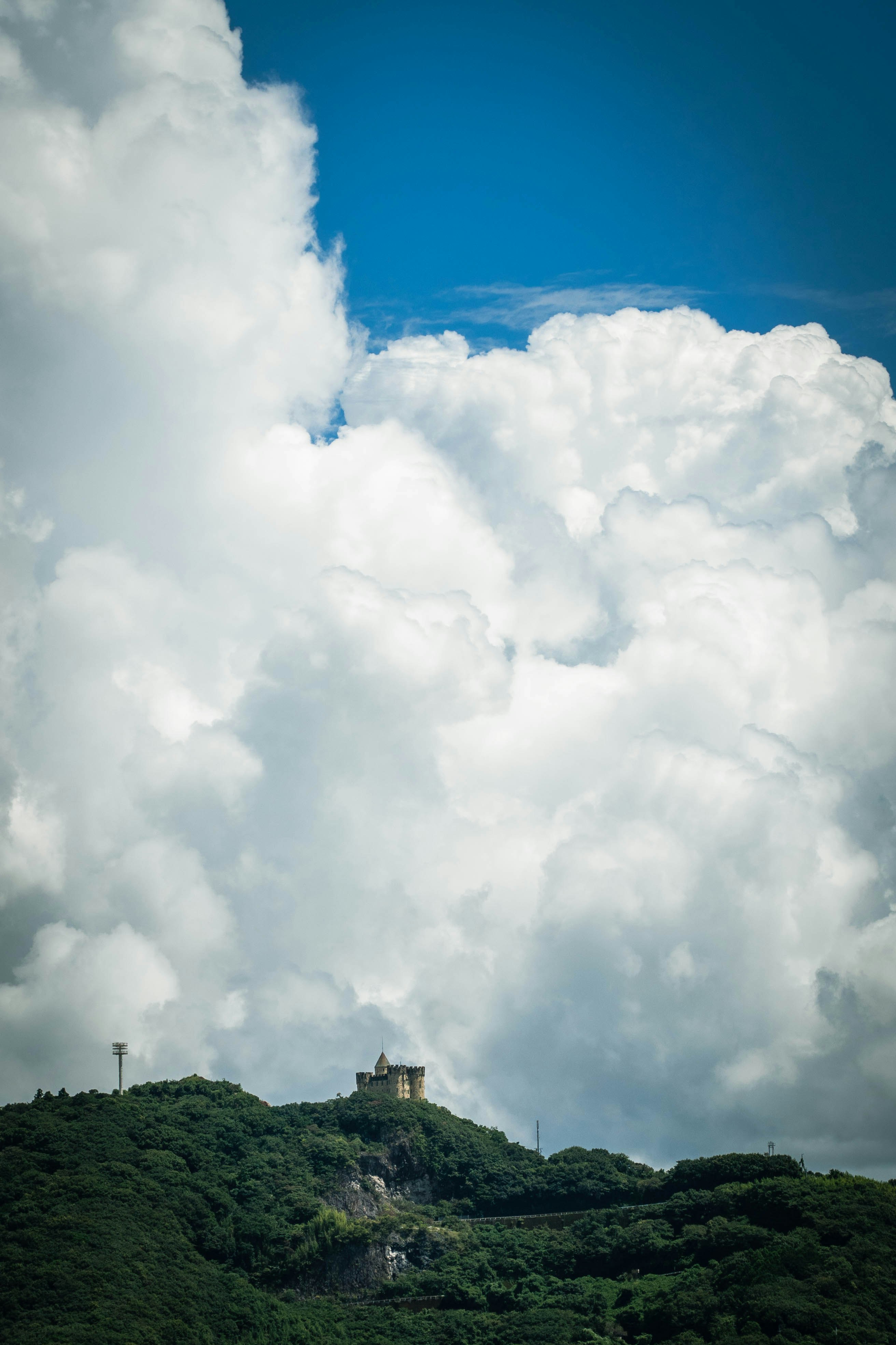 雲が広がる空と緑の丘に建つ灯台のある風景