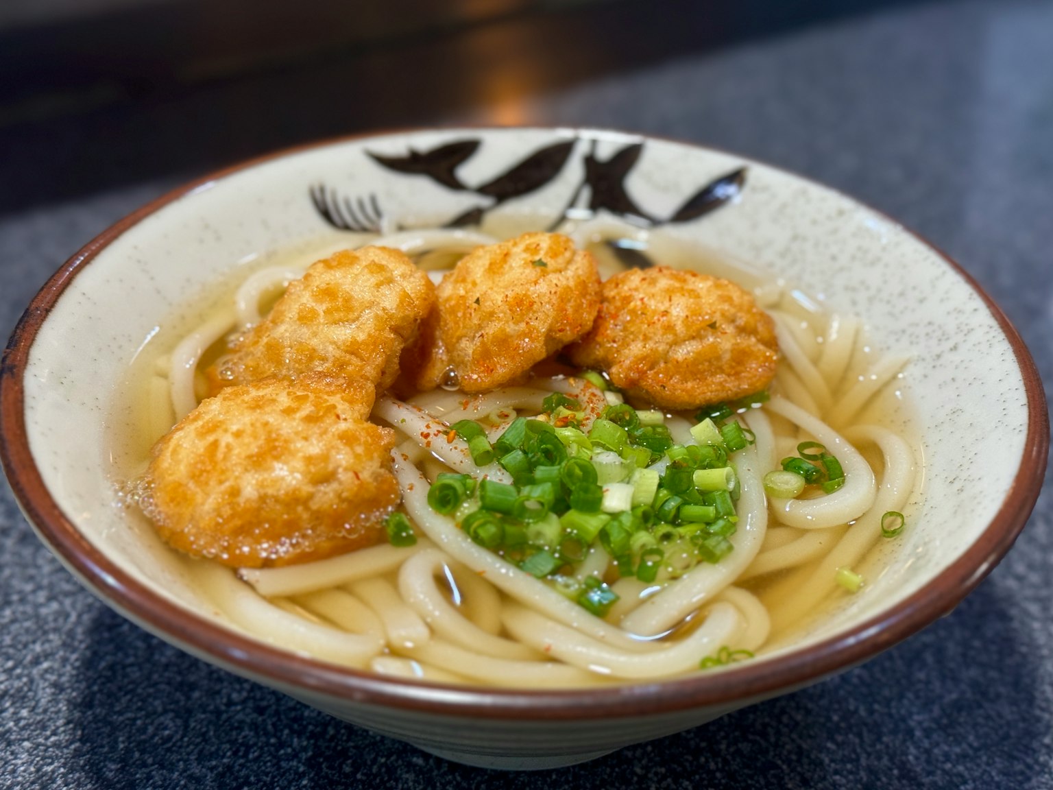 Mangkuk mie udon dengan tahu goreng dan bawang hijau