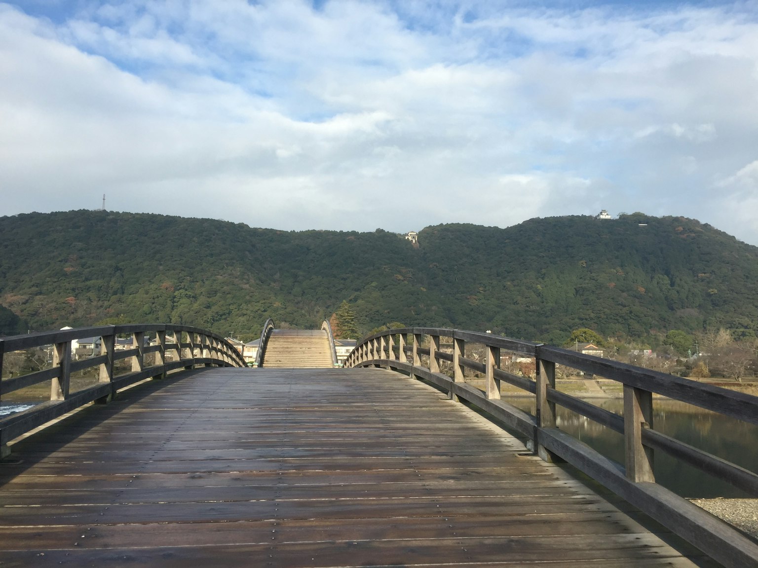 Szenische Aussicht auf eine Holzbrücke, die zu grünen Hügeln unter einem bewölkten Himmel führt