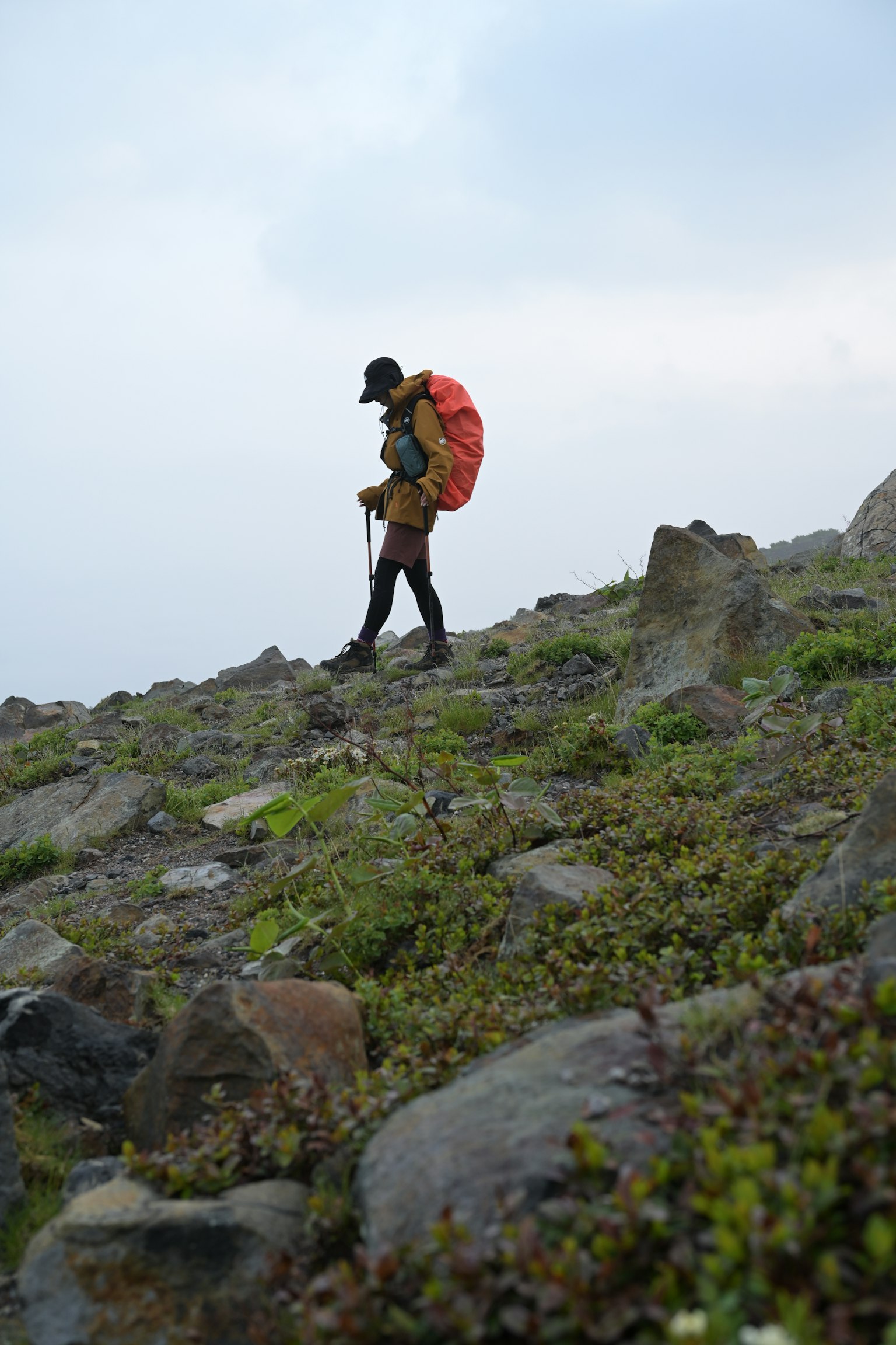 Ein Wanderer, der an einem felsigen Hang mit einem orangefarbenen Rucksack geht