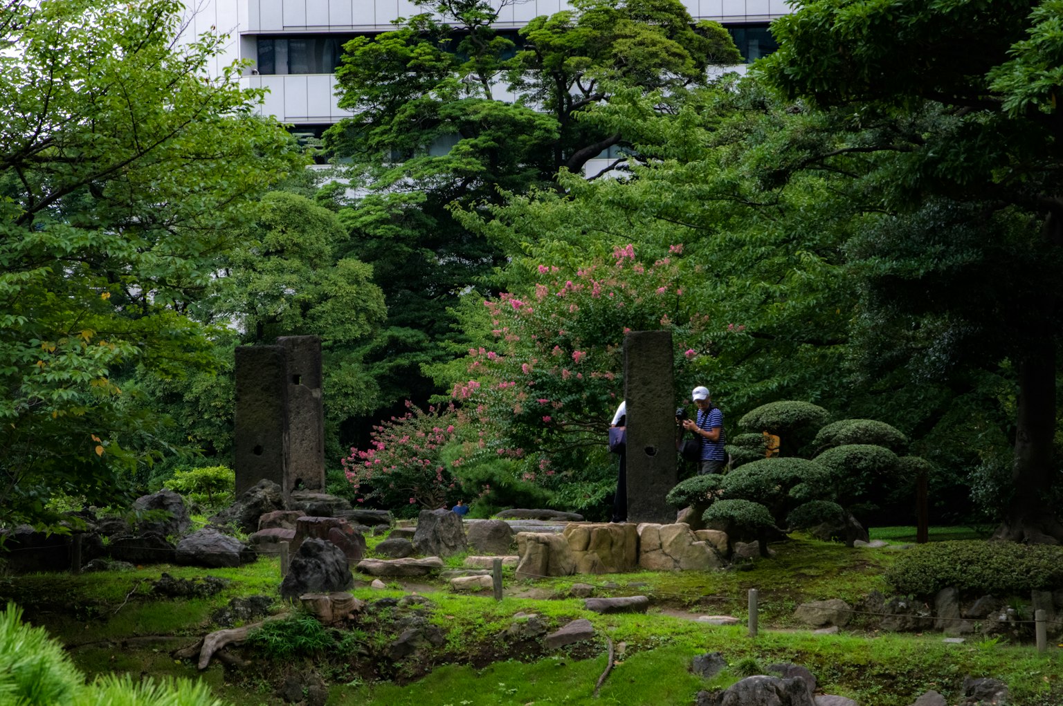 Des personnes se tenant dans un jardin luxuriant avec des sculptures en pierre visibles