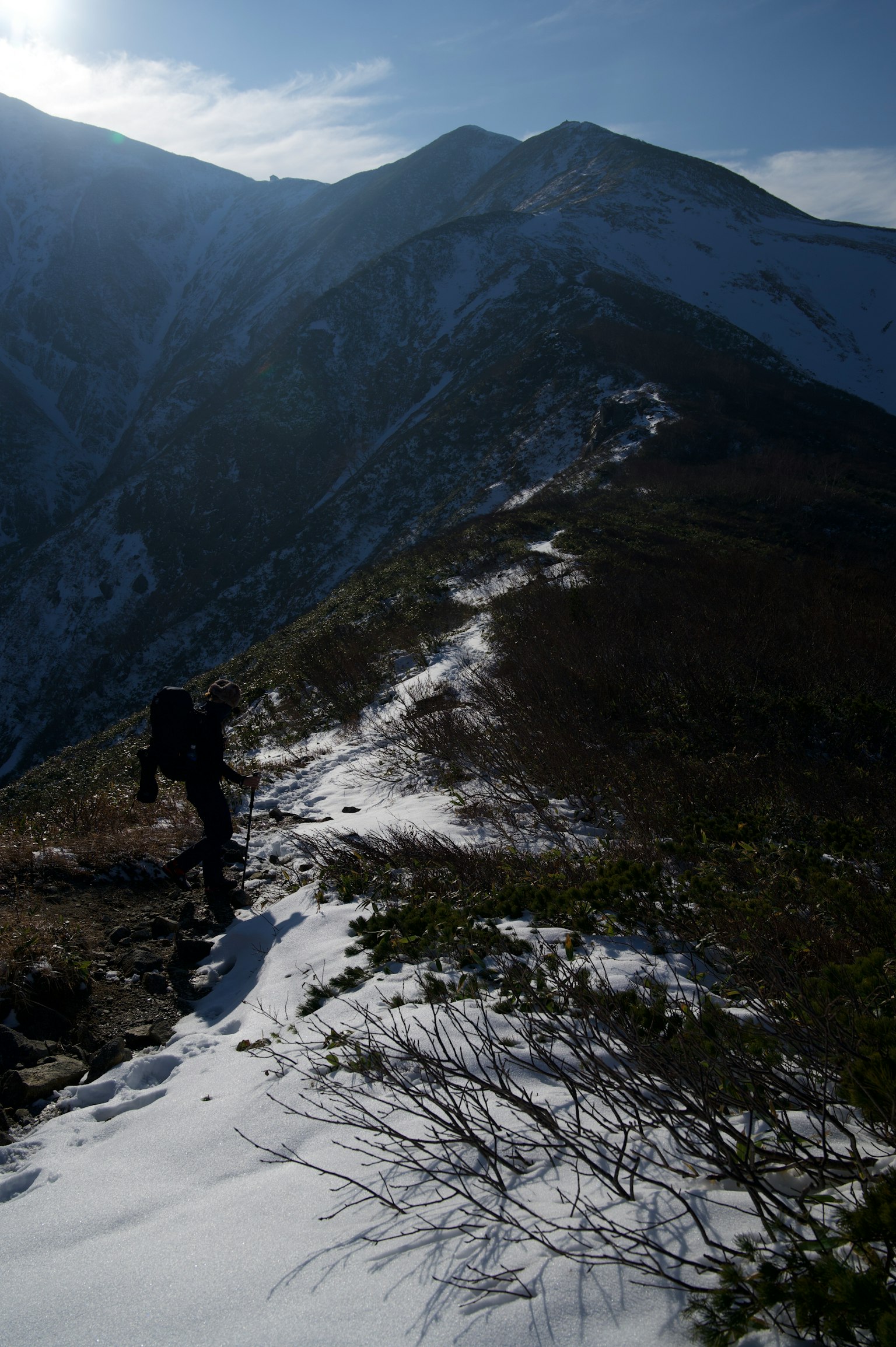 Silhouette of a hiker walking on a snowy mountain path with rugged peaks