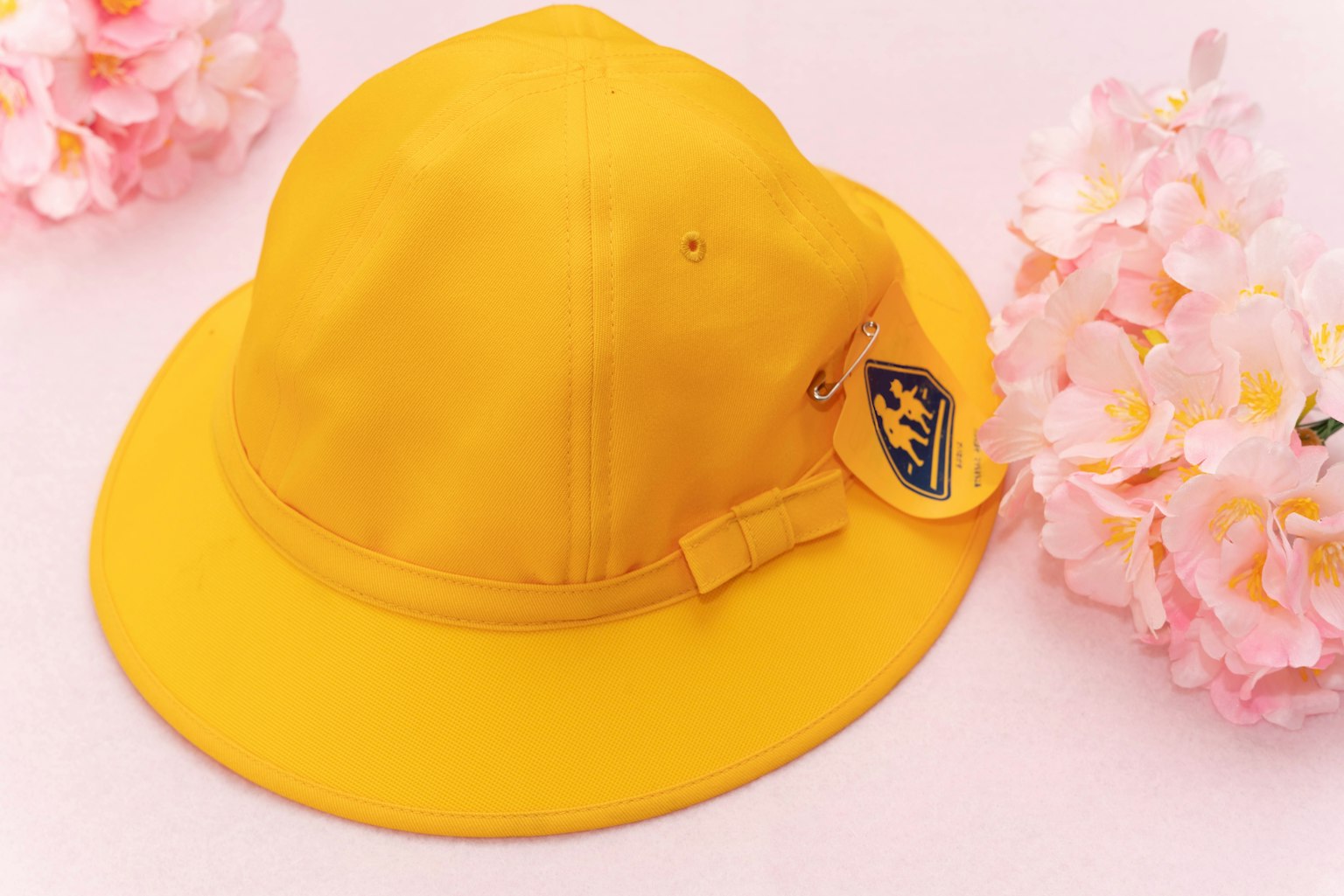 Helle gelbe Mütze neben rosa Blumen platziert