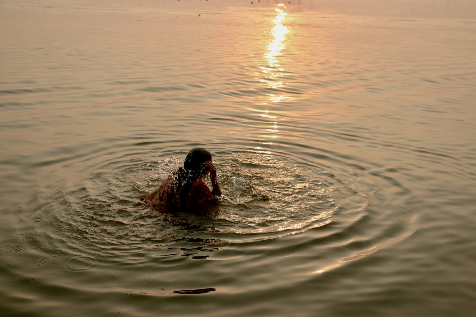 Eine Frau betet im Wasser mit einem Sonnenuntergang im Hintergrund