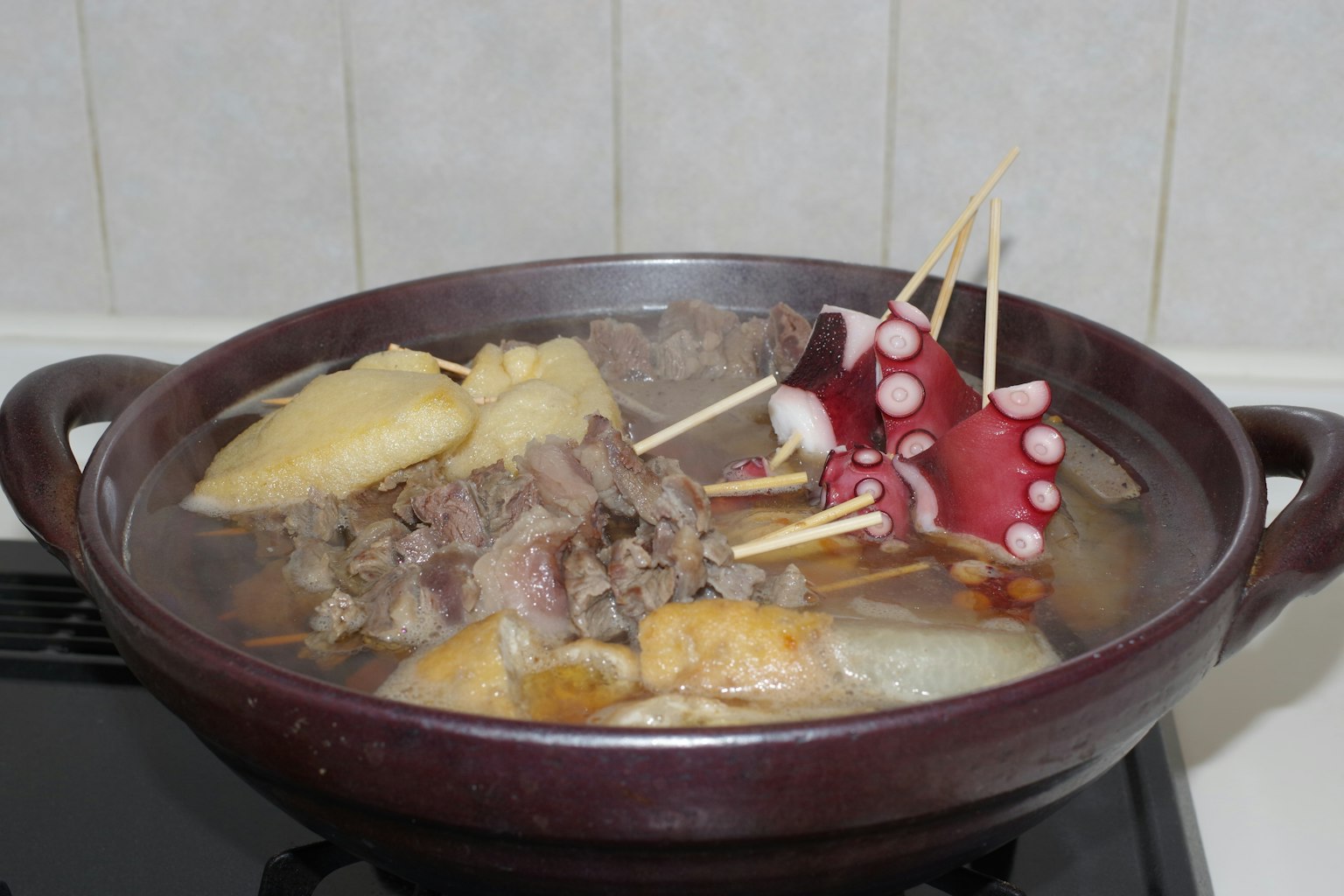 Ein Topf mit heißer Suppe mit verschiedenen Fleisch- und Gemüsesorten, darunter gegrillter Oktopus und Rettich