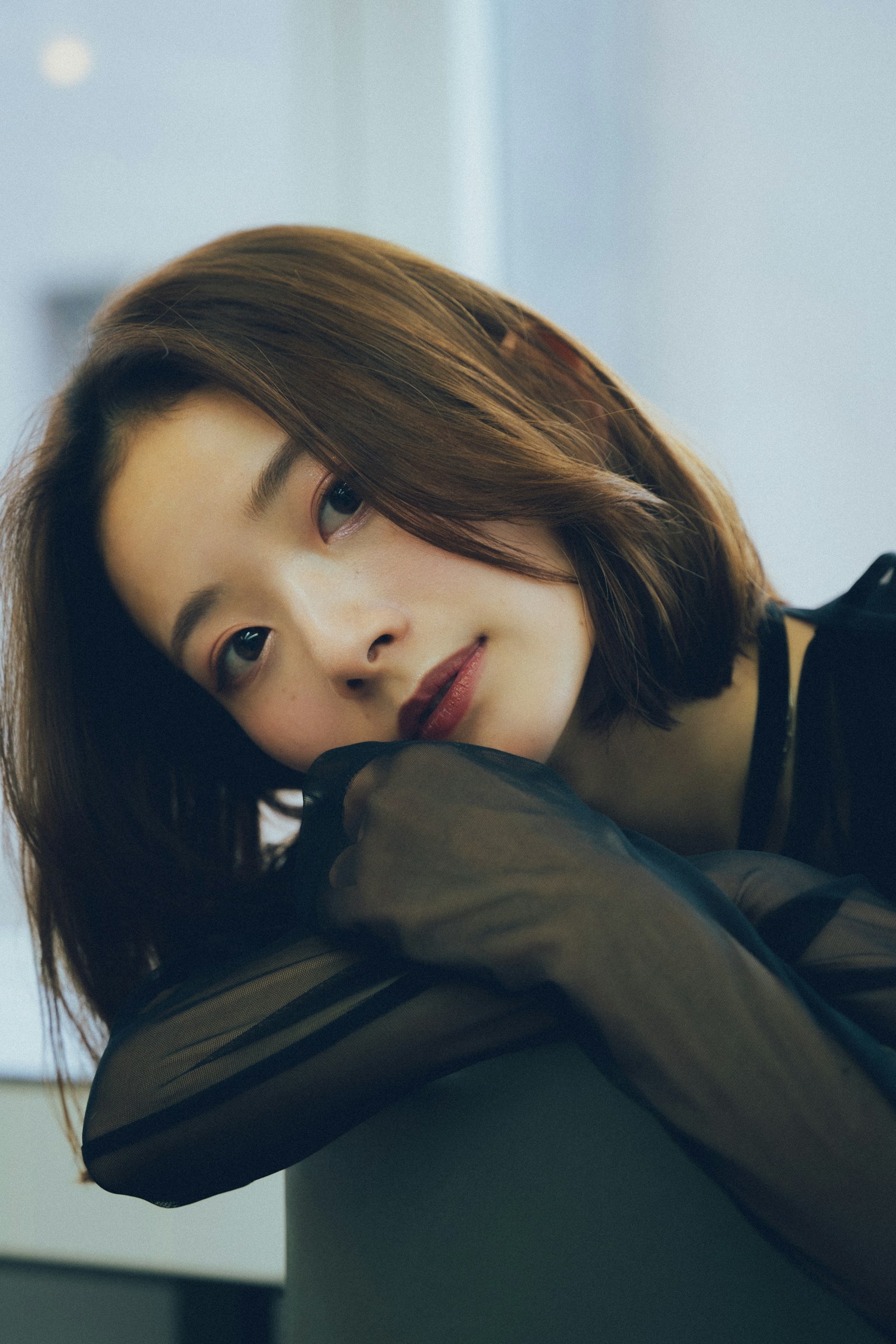 A young woman in a black outfit with shoulder-length hair resting her chin on her arm looking softly at the camera