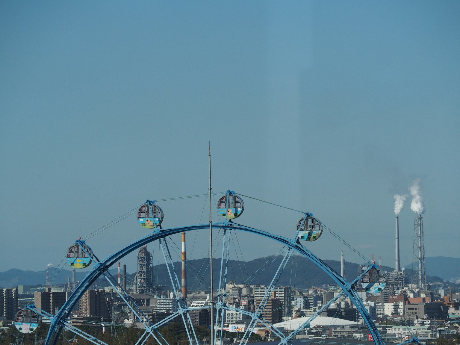 Pemandangan kota dengan roda ferris biru dan cerobong asap industri