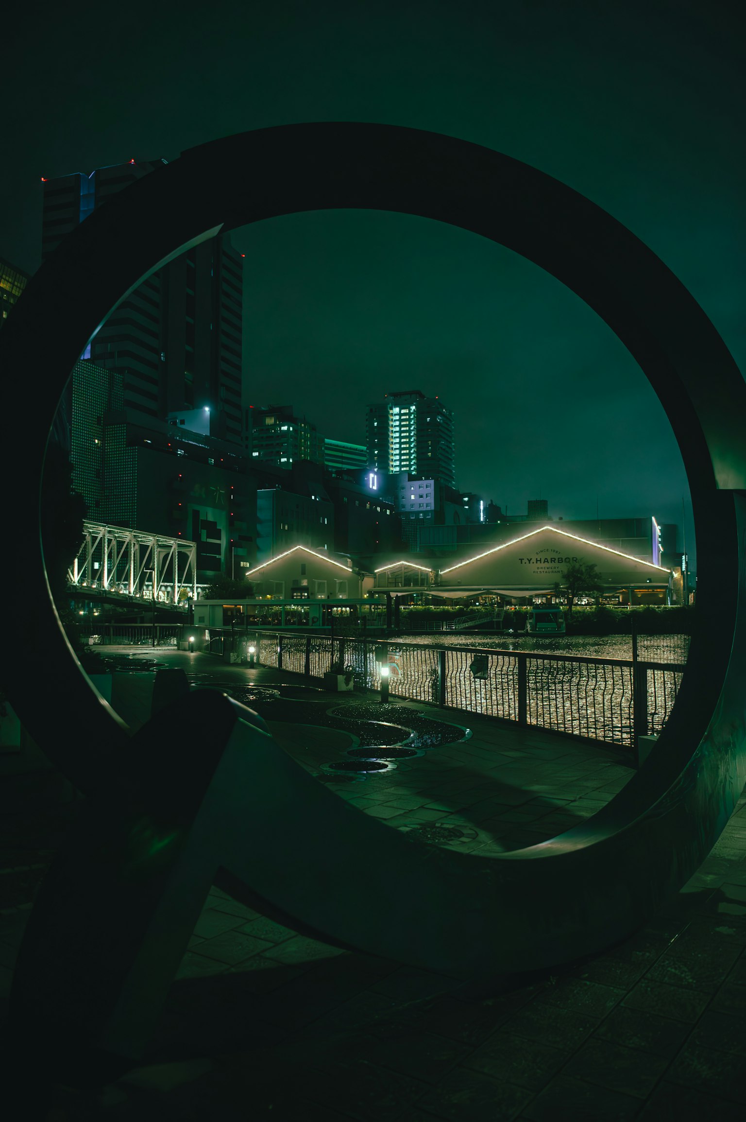 Escena urbana nocturna enmarcada por una estructura circular Edificios brillantes y una iluminación verde son impactantes