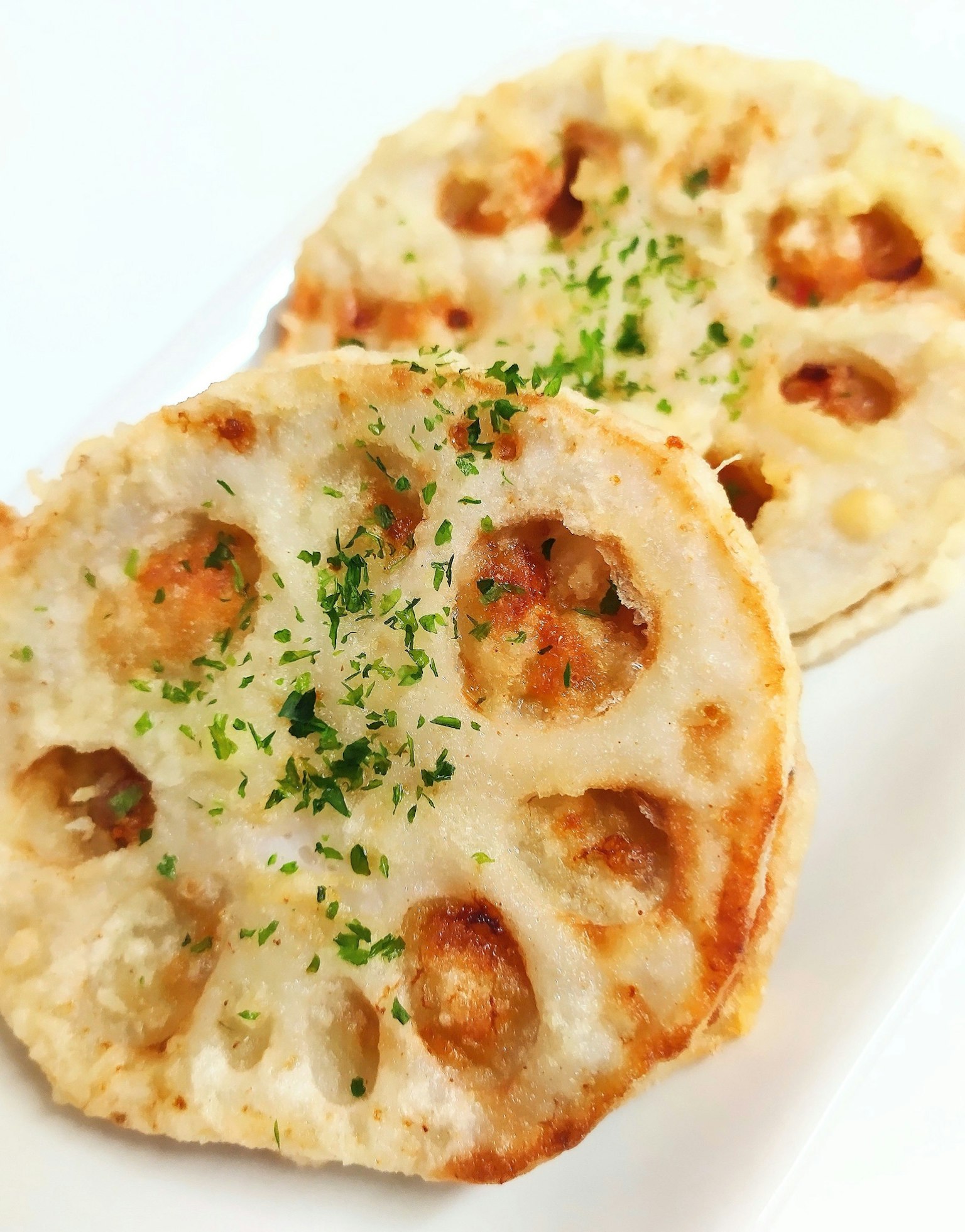 Zwei Scheiben gegrillte Lotuswurzel mit grünen Kräutern auf einem weißen Teller