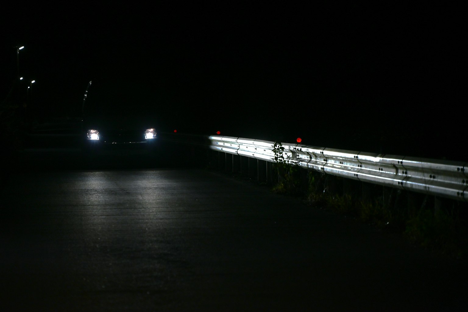 Autolichter beleuchten eine dunkle Straße mit reflektierendem Schutzgeländer