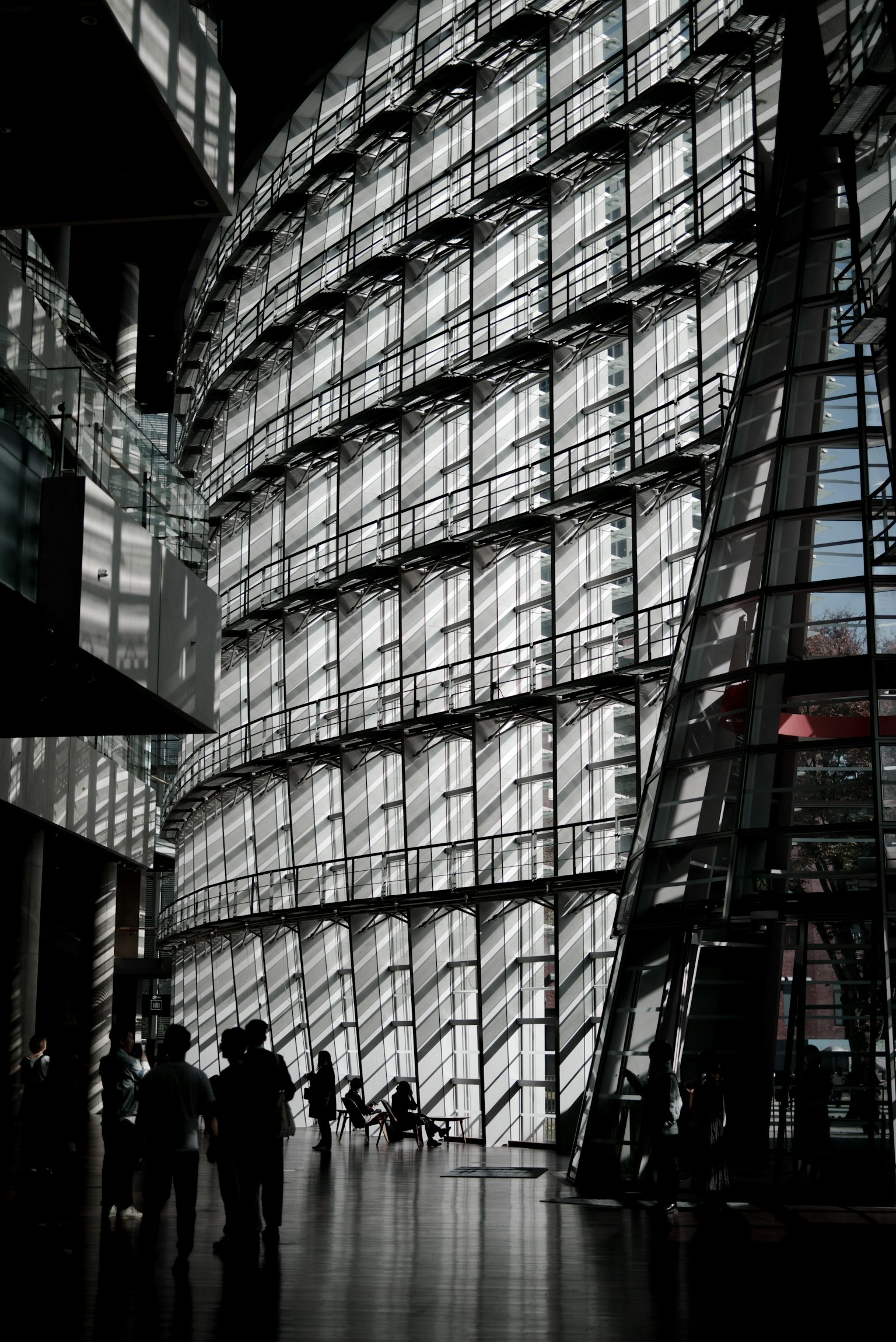 Innenraum eines modernen Gebäudes mit großen Glaswänden und silhouettierten Figuren