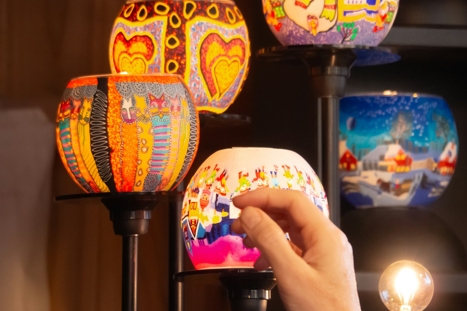 Sebuah tangan menjangkau lampu dekoratif berwarna-warni dalam pameran seni