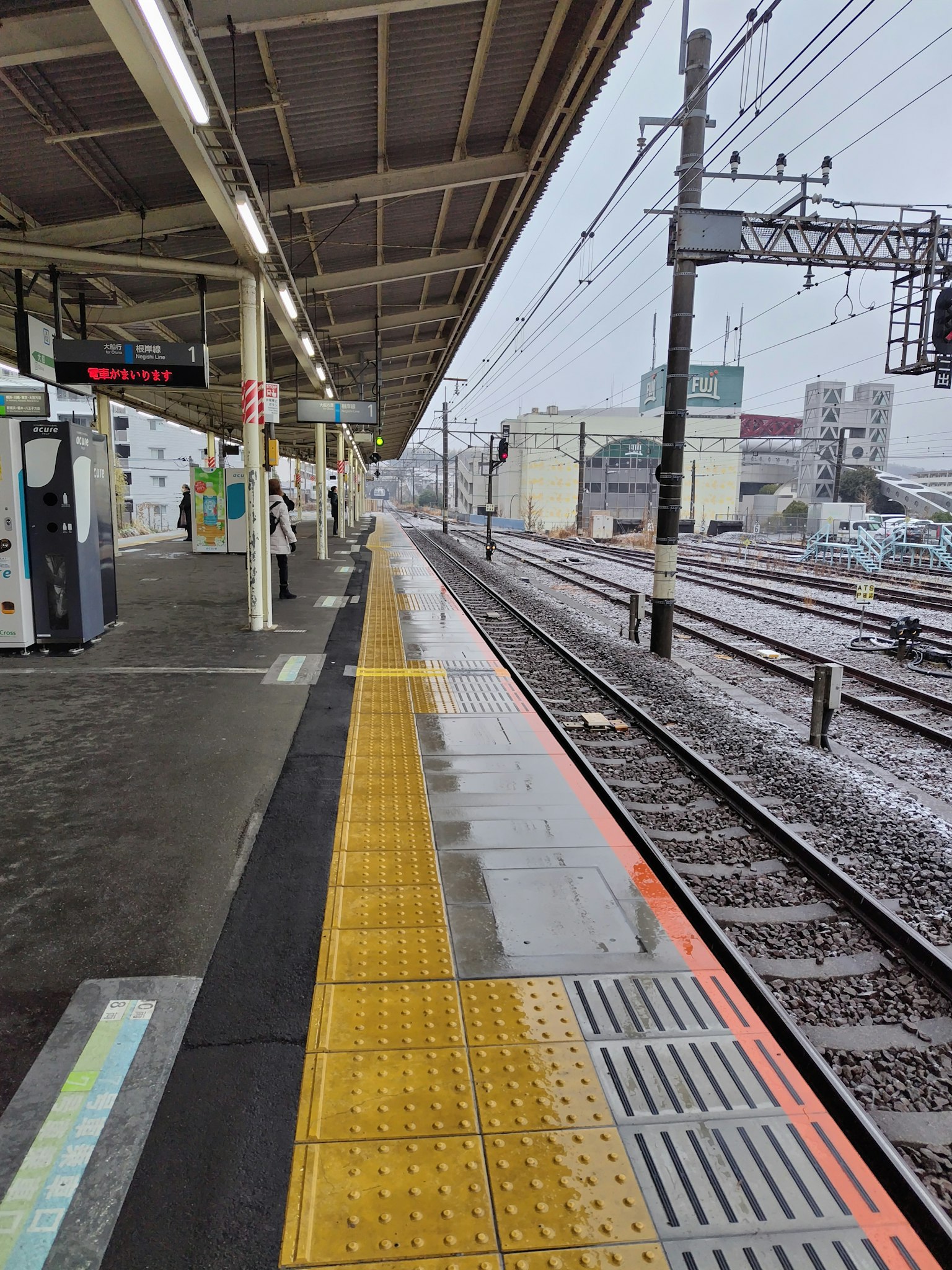 Plateforme de gare avec pavage tactile jaune et voies ferrées sous la pluie