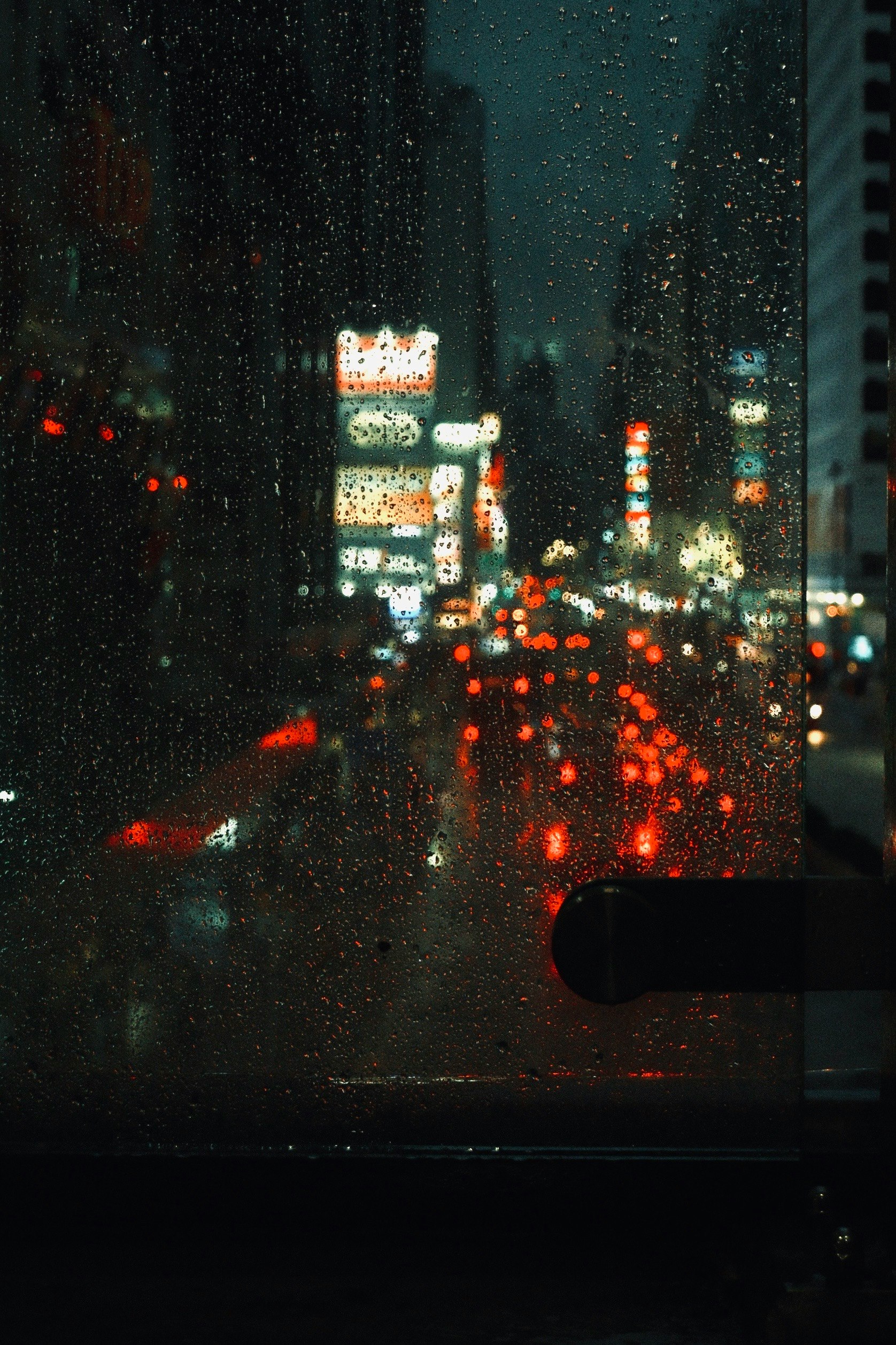 雨粒の窓越しににぎわう夜の街並み