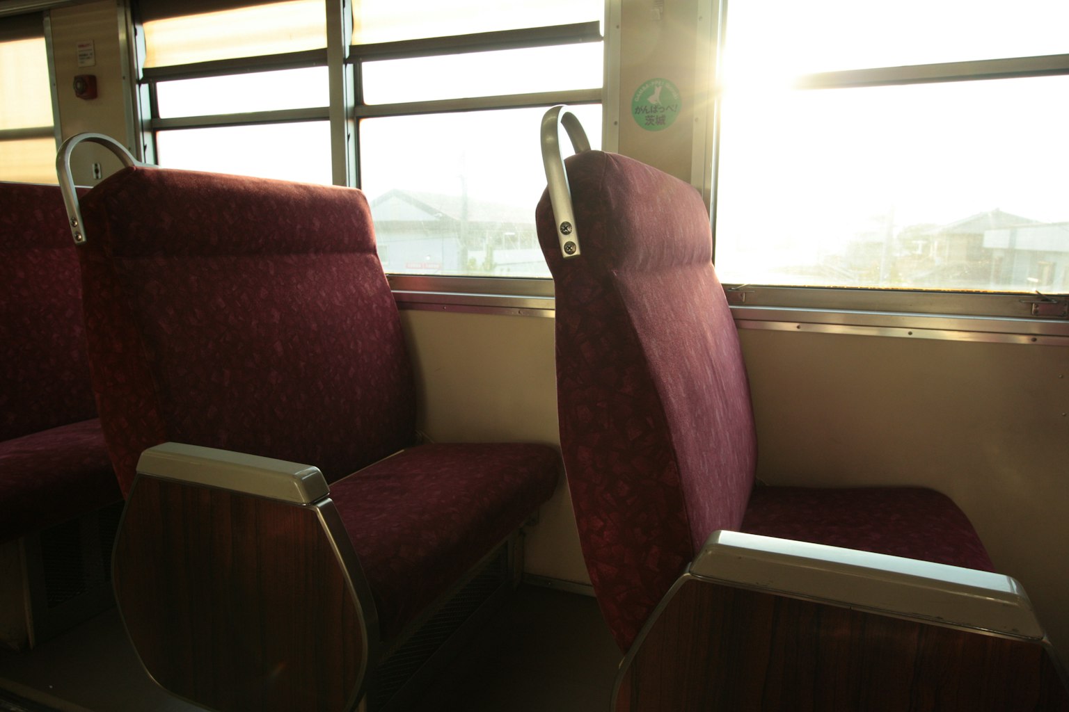 Vista interior de un tren con asientos burdeos y luz solar