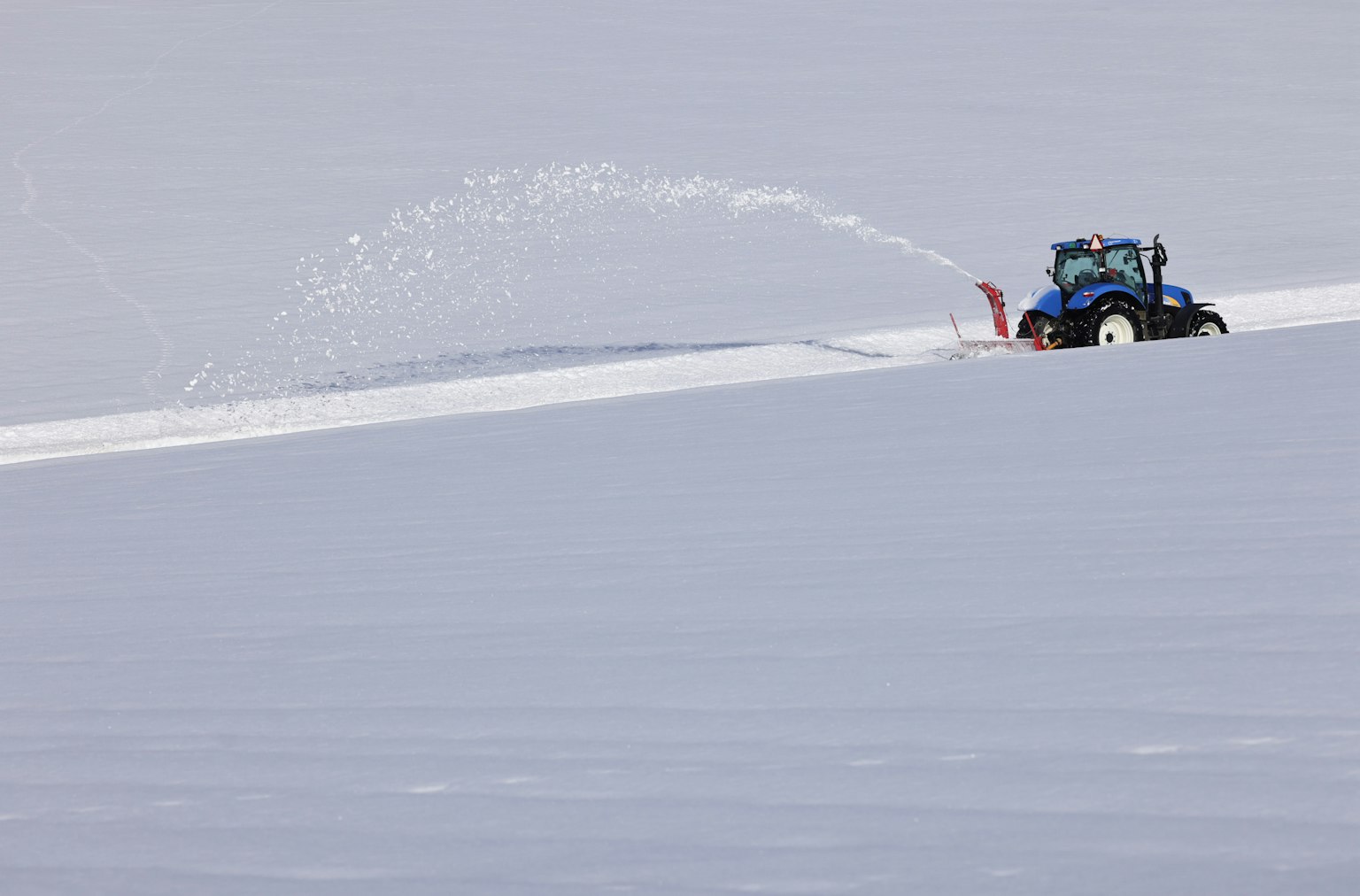 Tracteur déneigeant avec un souffleuse à neige dans un paysage enneigé