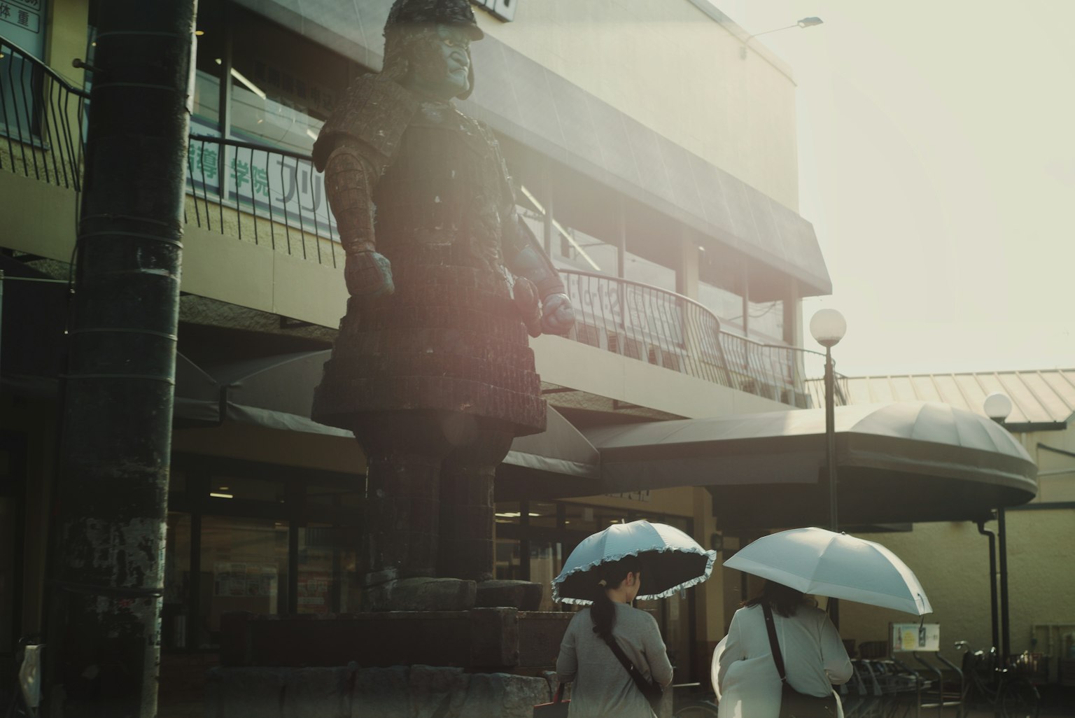 两名女性在雕像前走着，手持雨伞