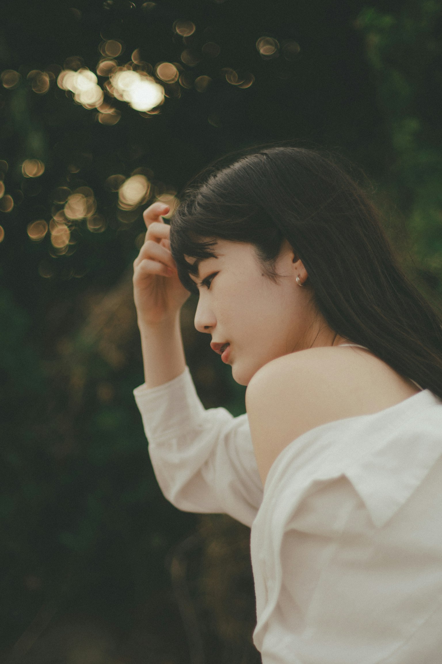 一名穿著白襯衫的女性側身看，背景為柔和的光線和綠色自然景觀