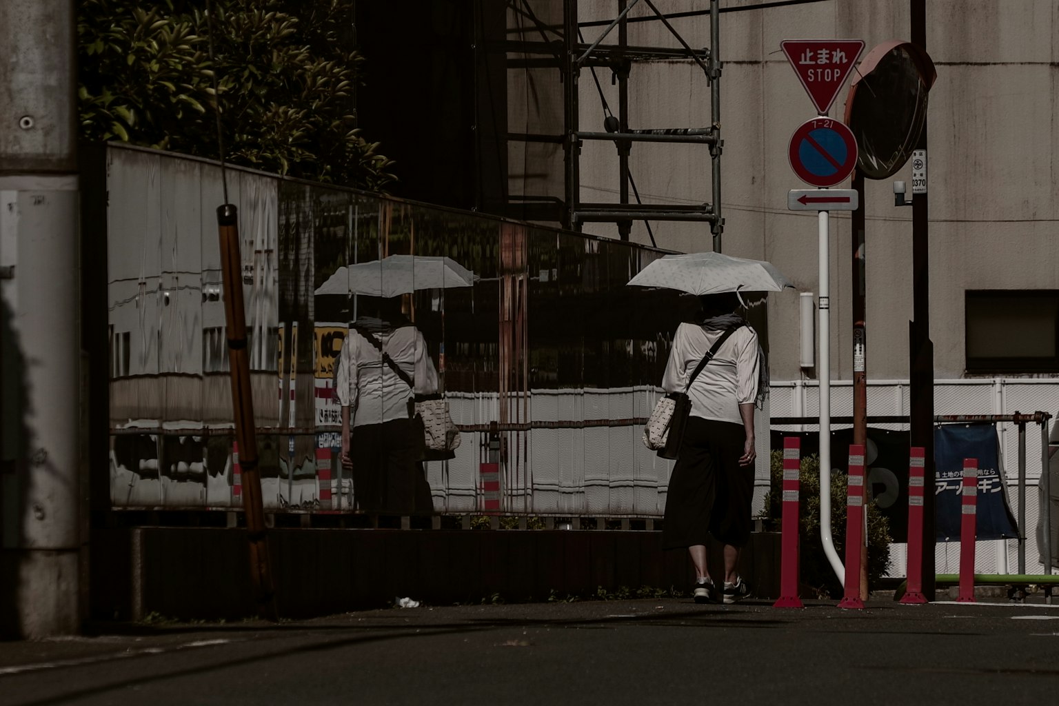 ผู้หญิงถือร่มสีขาวยืนอยู่ที่มุมถนนพร้อมกับการสะท้อนที่มองเห็นได้