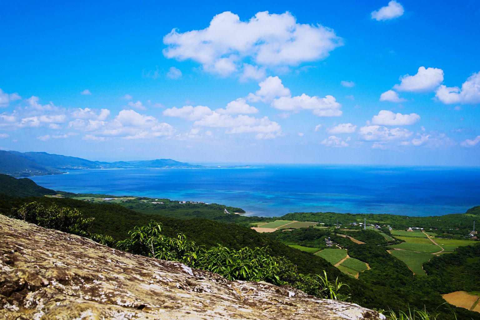 Vista escénica del océano azul y nubes colinas verdes y rocas en primer plano