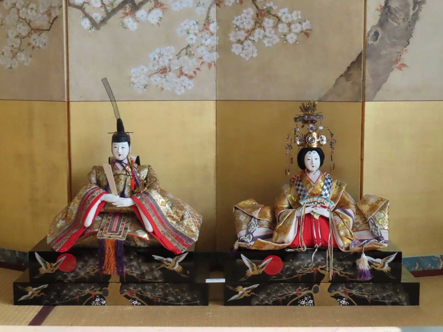 Deux poupées hina assises sur un fond doré, figure masculine à gauche et figure féminine à droite, ornées de vêtements traditionnels colorés