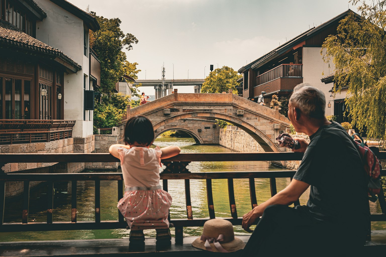 Una ragazza e un uomo anziano osservano un ponte circondato da edifici tradizionali e un corso d'acqua tranquillo