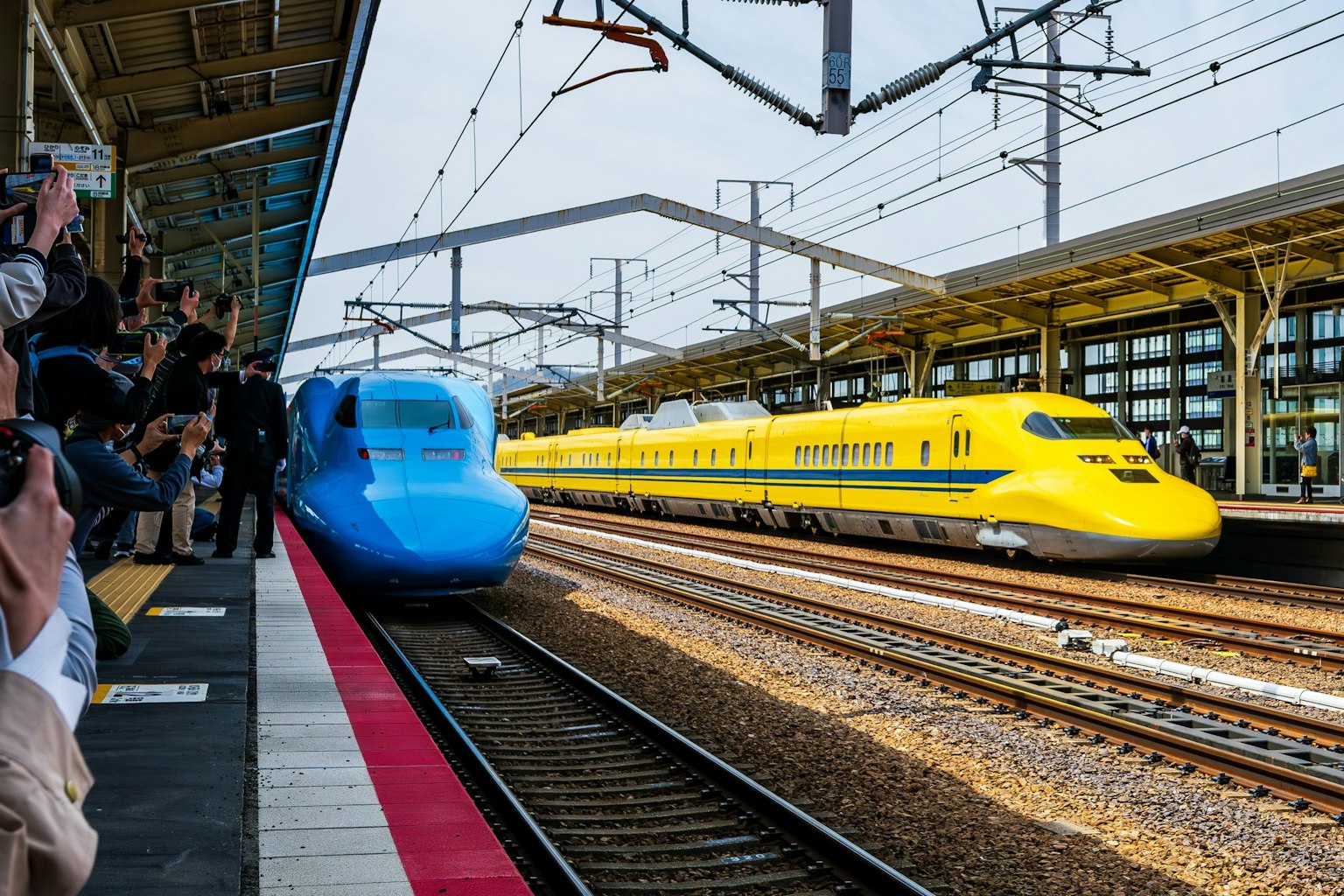 Blue Shinkansen and yellow Shinkansen passing each other at the station
