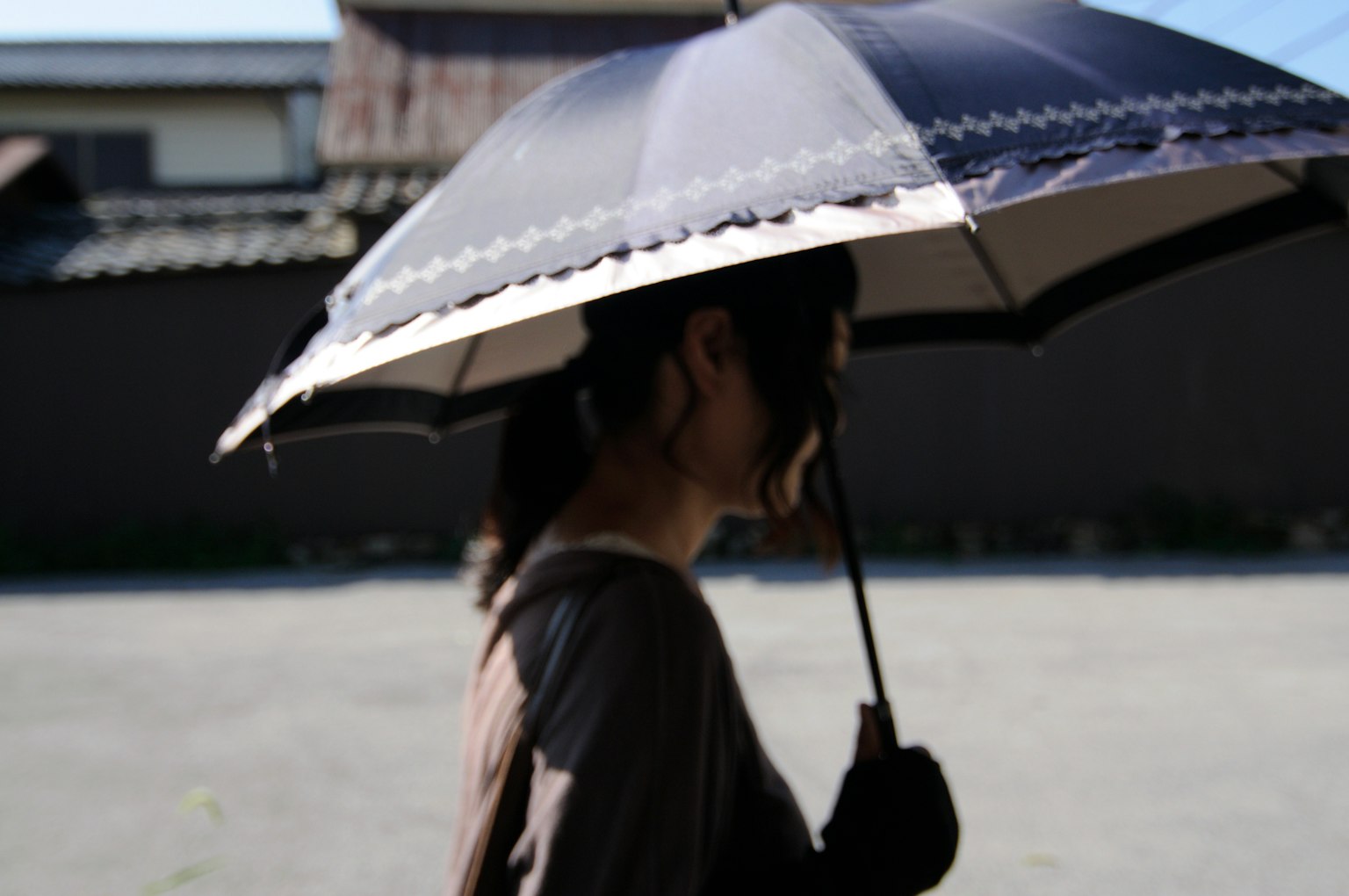 Profilo laterale di una donna che tiene un parasole mentre cammina al sole