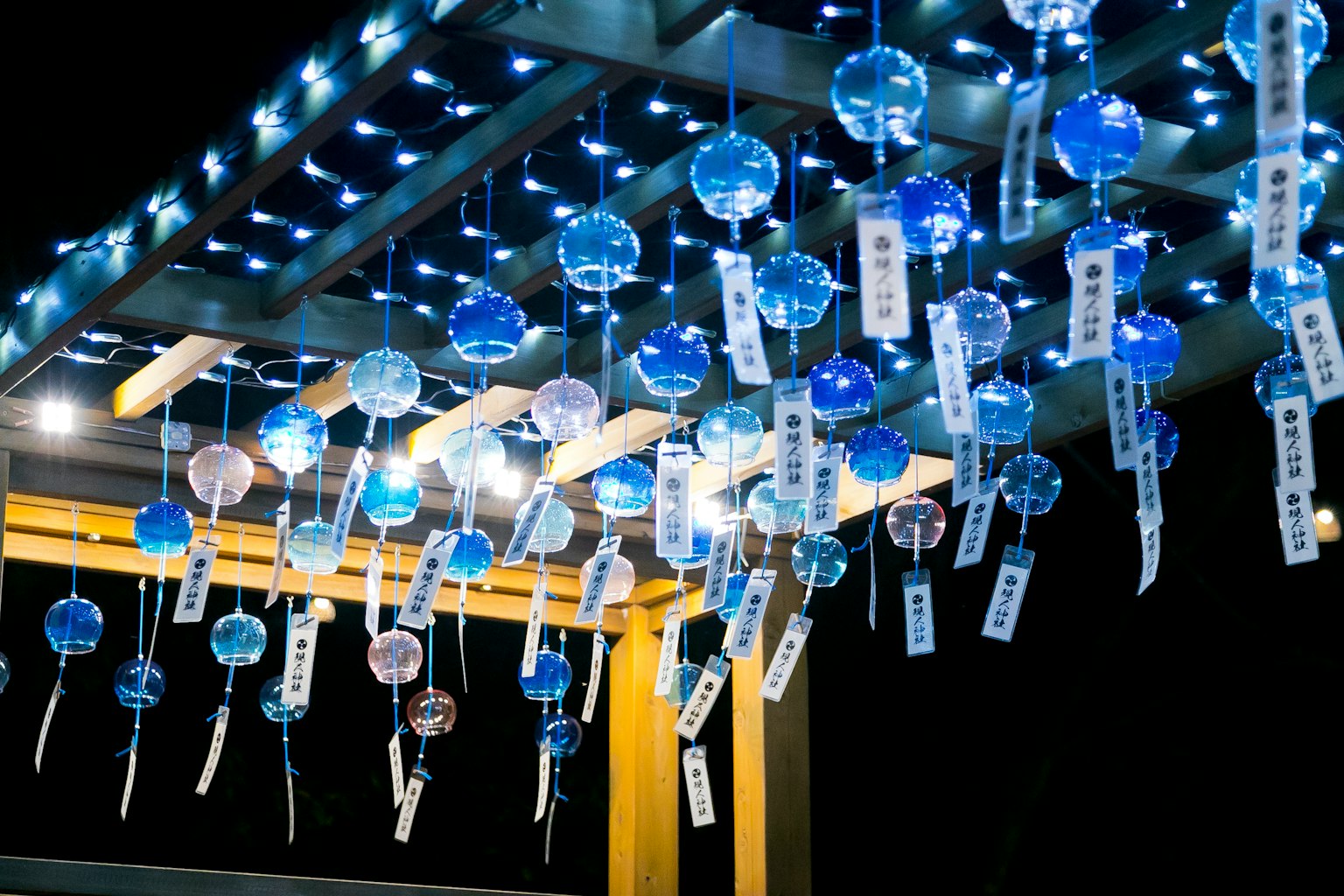 Campanas de viento azules colgando bajo un techo iluminado por luces nocturnas