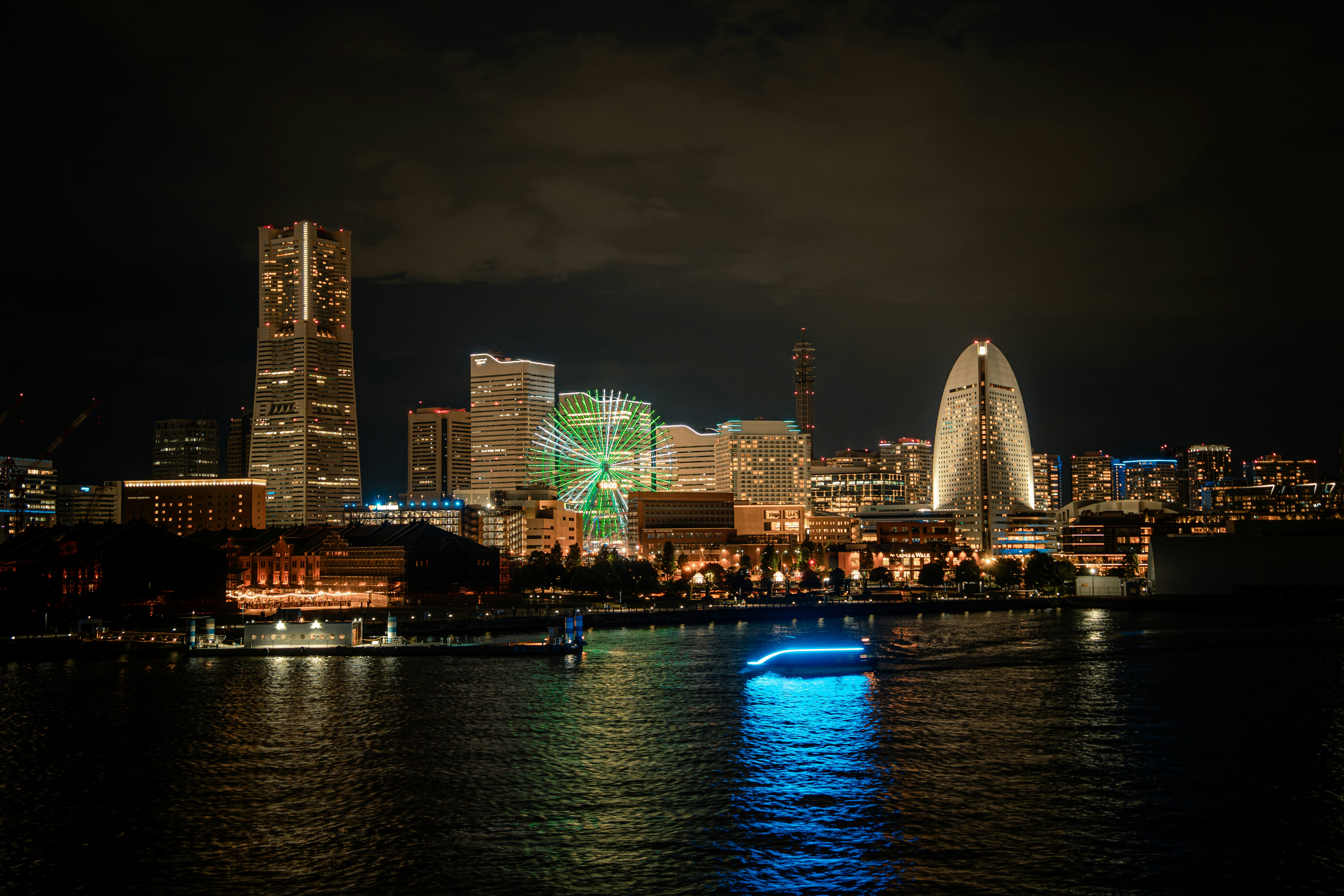 Horizonte nocturno junto a un río con rascacielos iluminados y una noria