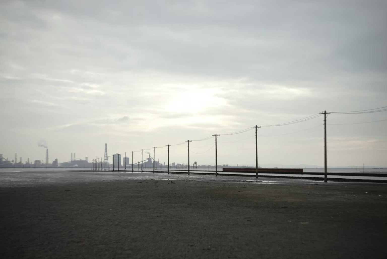 Paesaggio industriale sotto un cielo nuvoloso con pali della luce e silhouette di fabbriche sullo sfondo