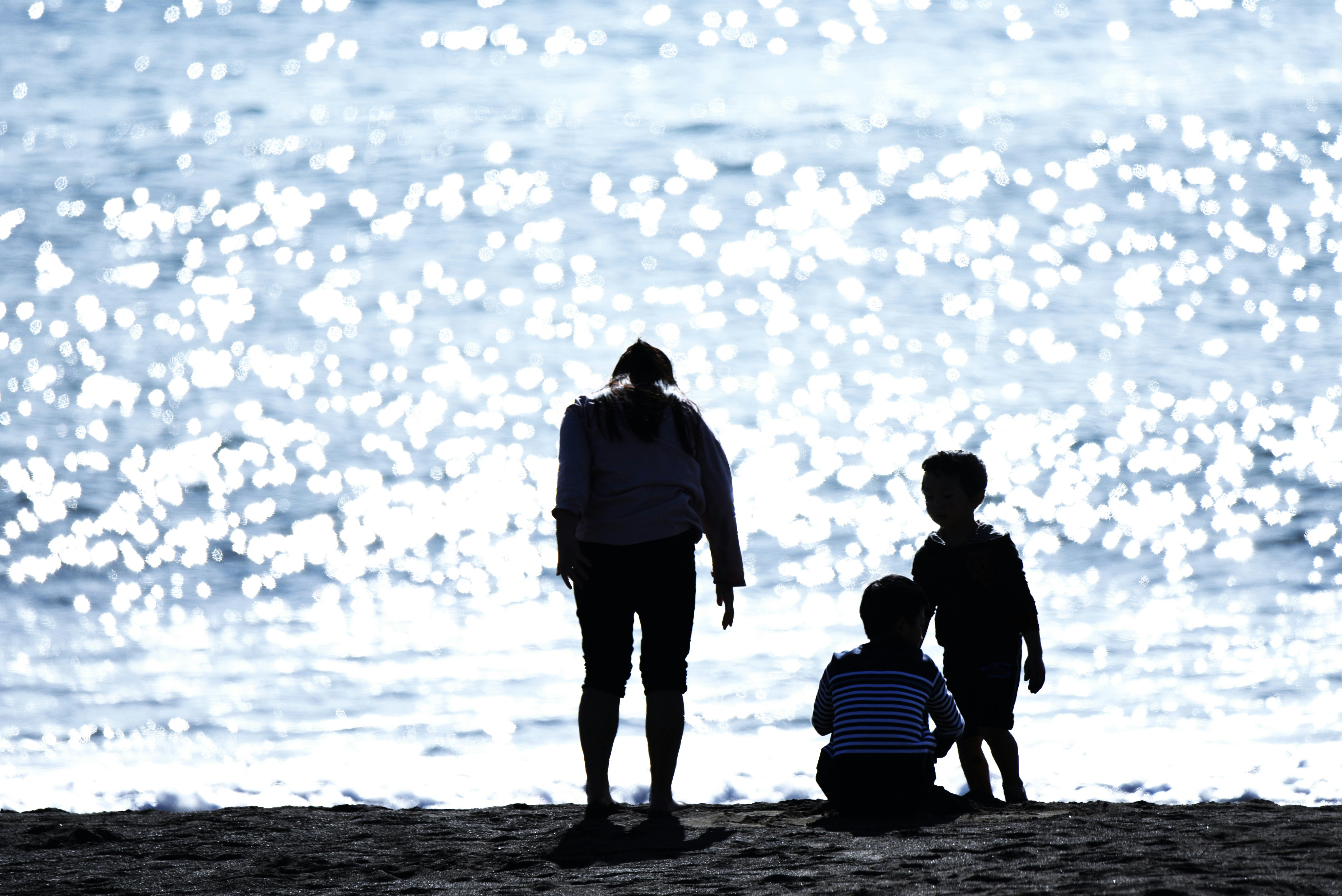 Beach silhouette of a parent and child with blurred ocean sparkle in the background