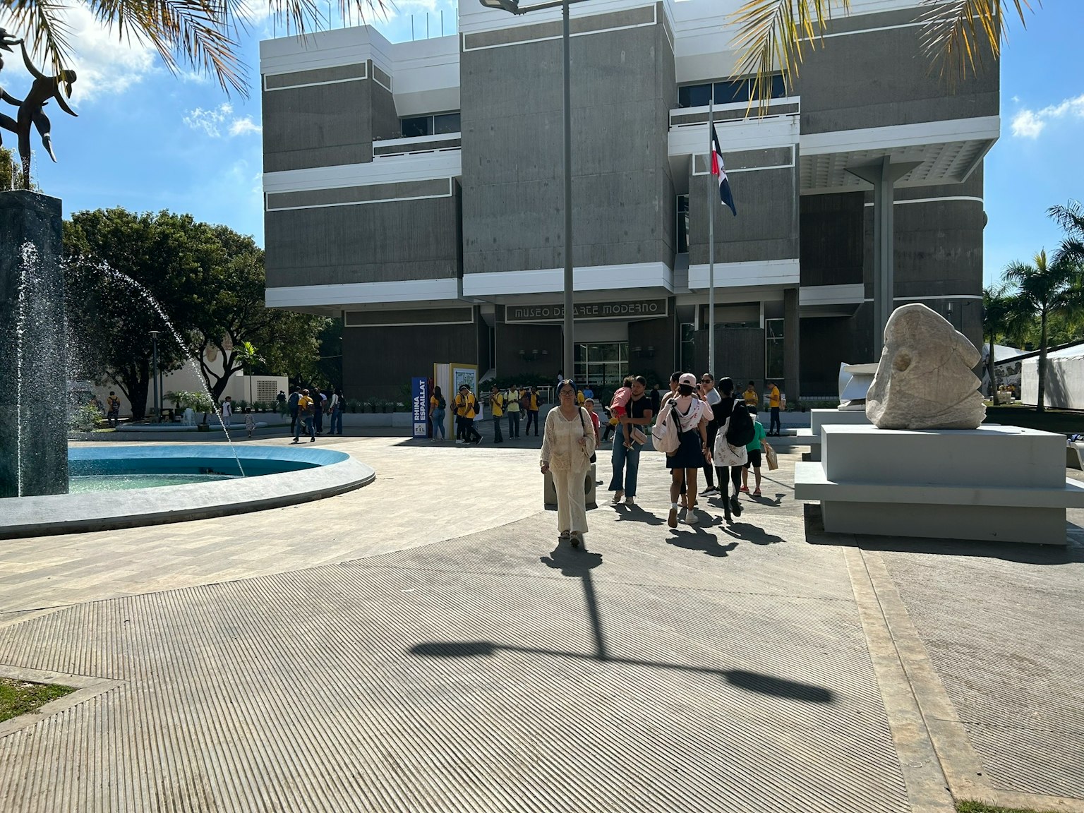 Orang-orang berkumpul di depan gedung modern dengan air mancur
