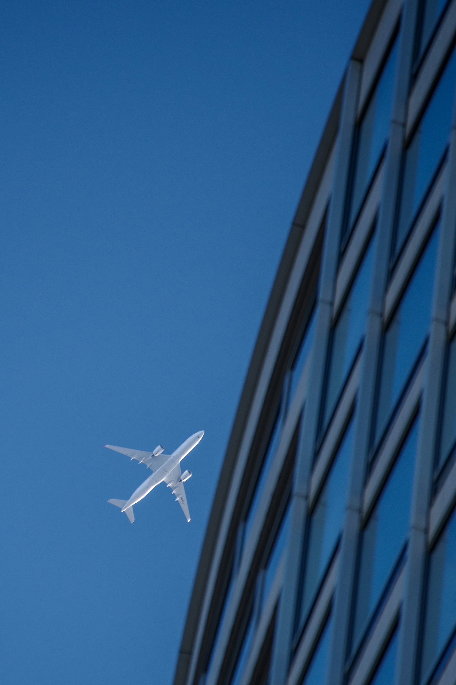 Flugzeug fliegt im blauen Himmel neben einem Glasgebäude