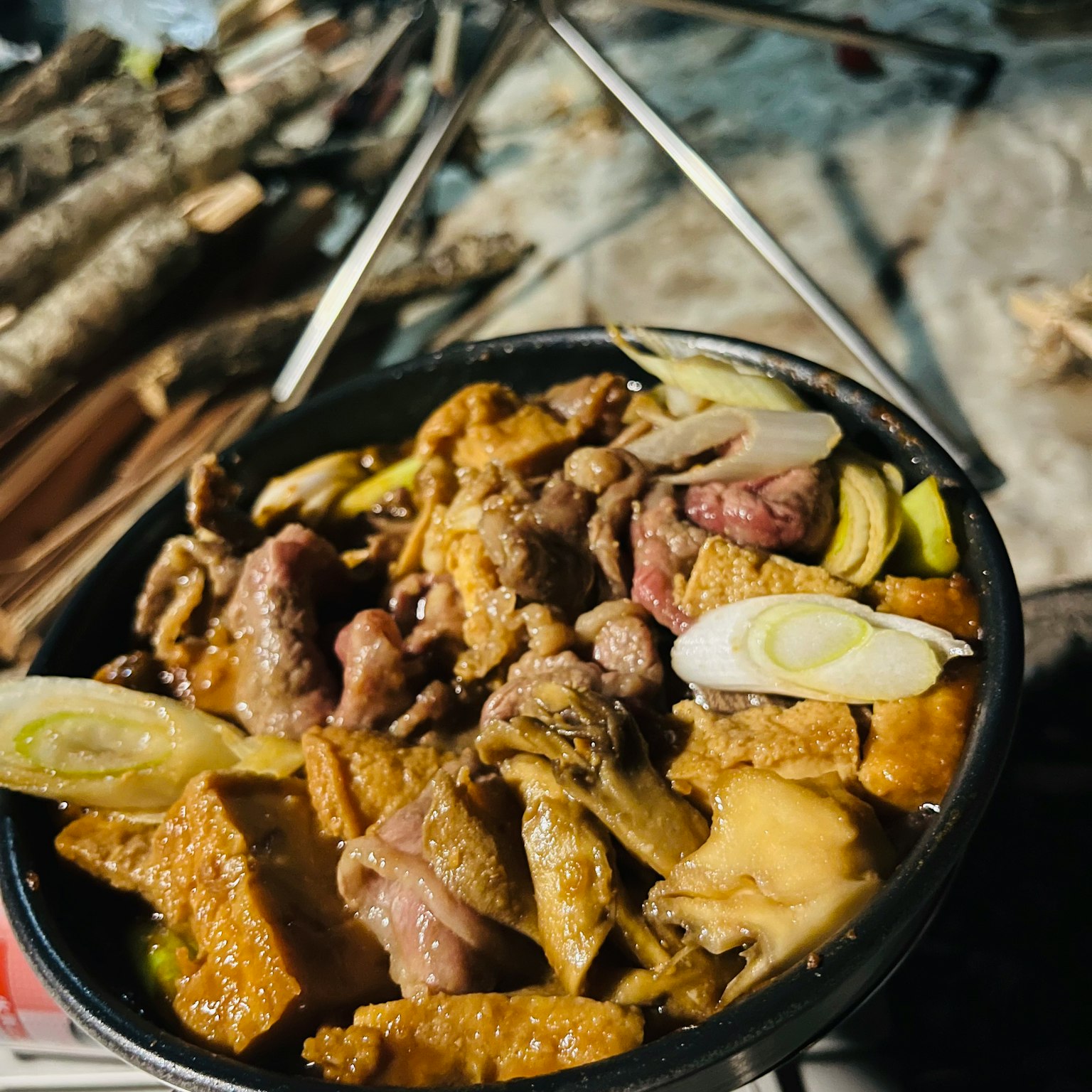 Un tazón de carne y cebolla verde con brochetas y leña al fondo