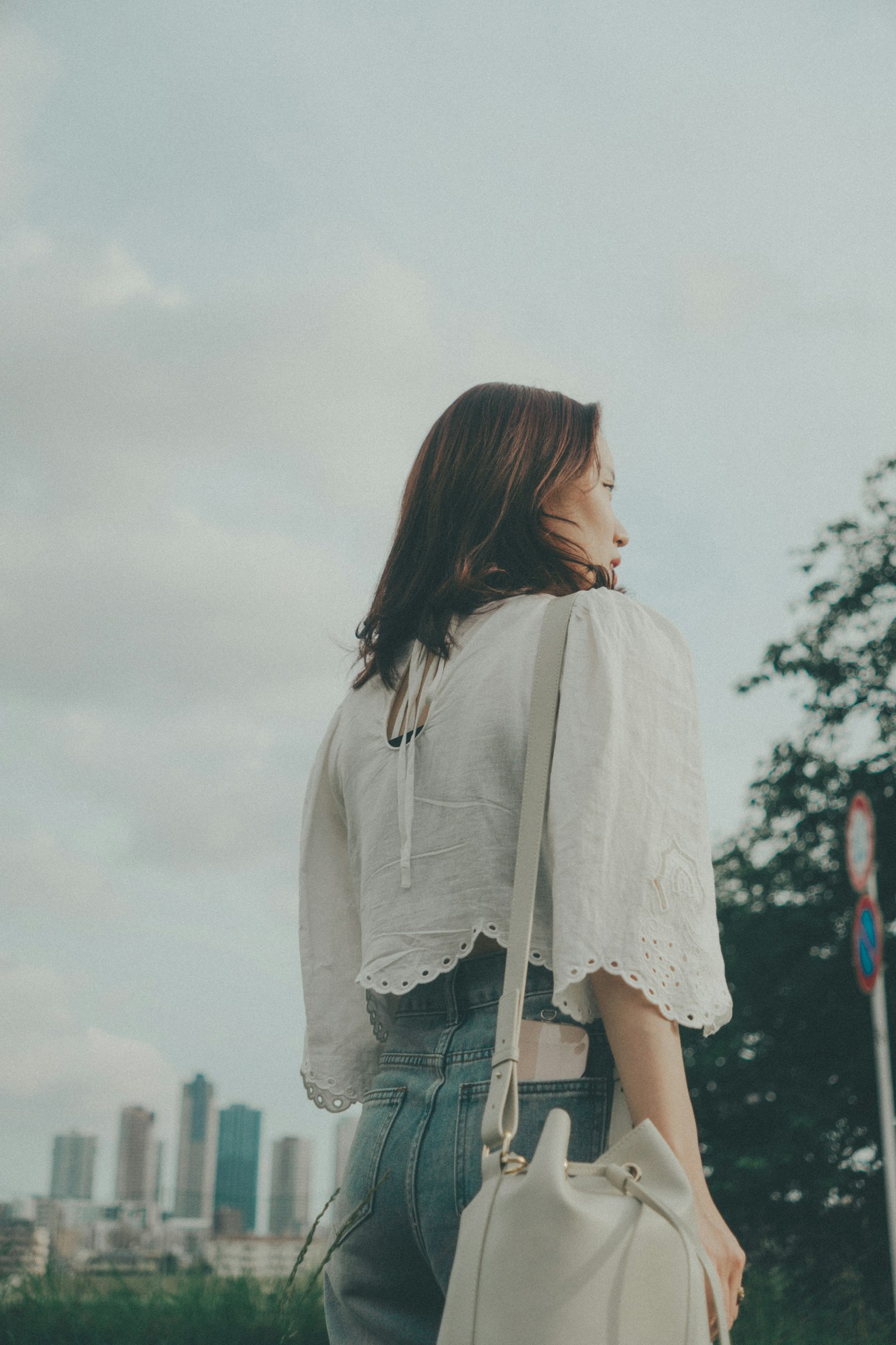 Una donna in blusa bianca e jeans sta in piedi con le spalle alla skyline della città
