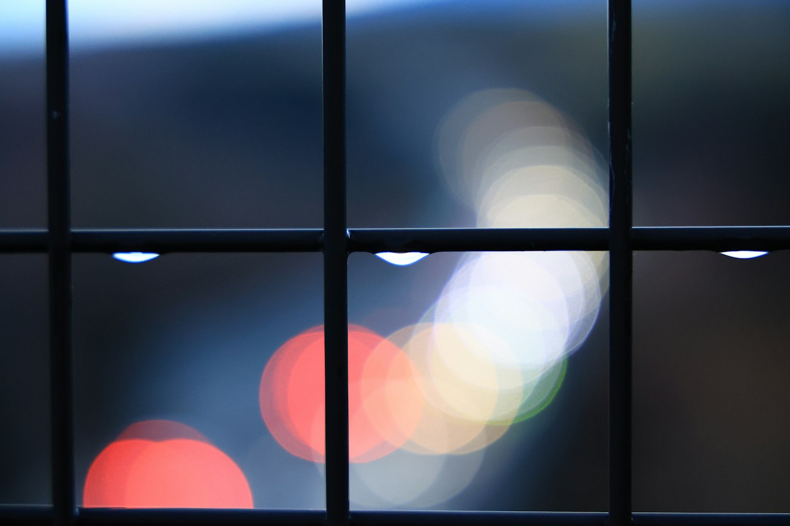 Verschwommene Lichter und Wassertropfen durch ein Fenster-Gitter gesehen