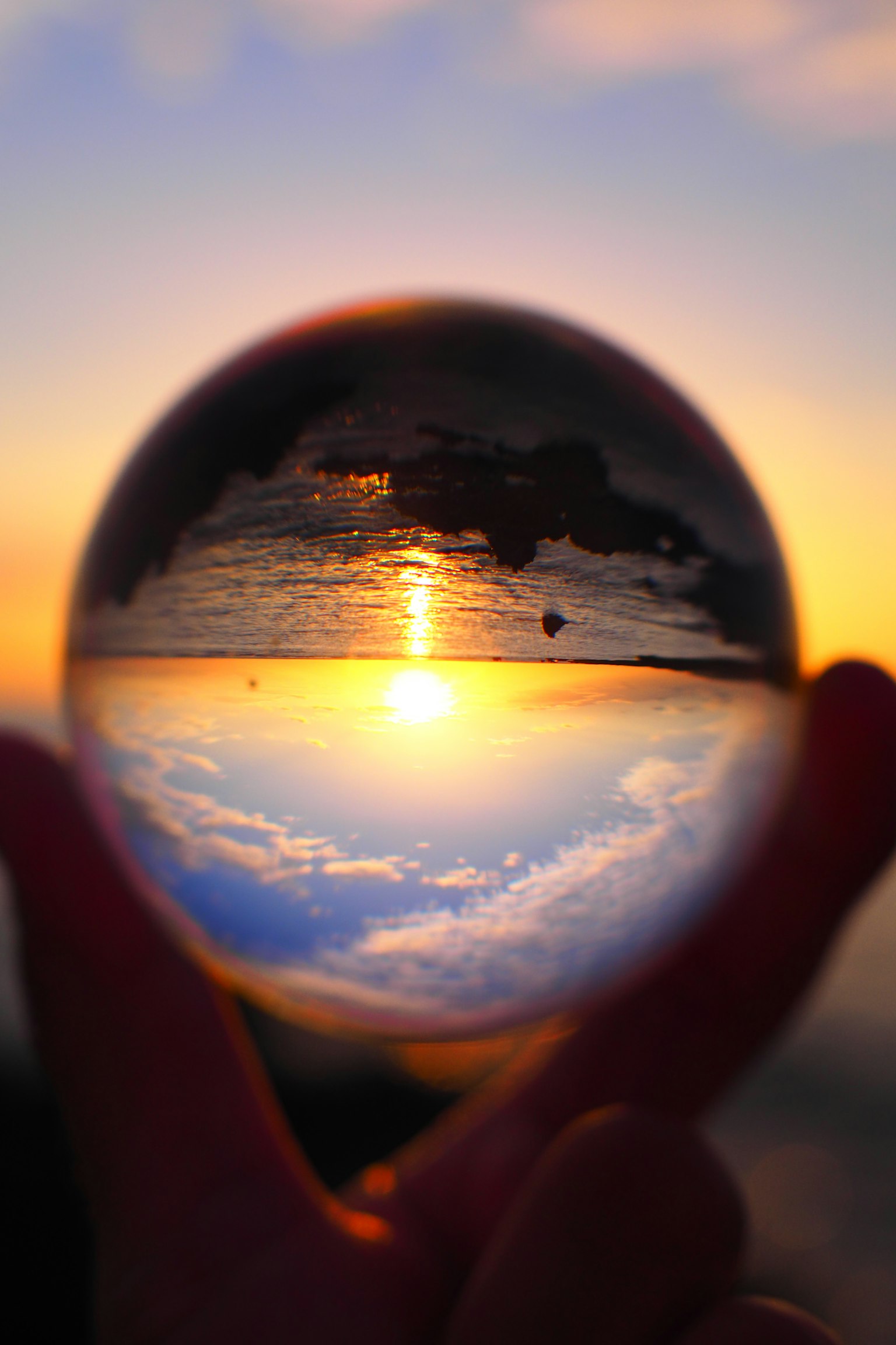 Una sfera di cristallo tenuta in mano che riflette un tramonto e il cielo