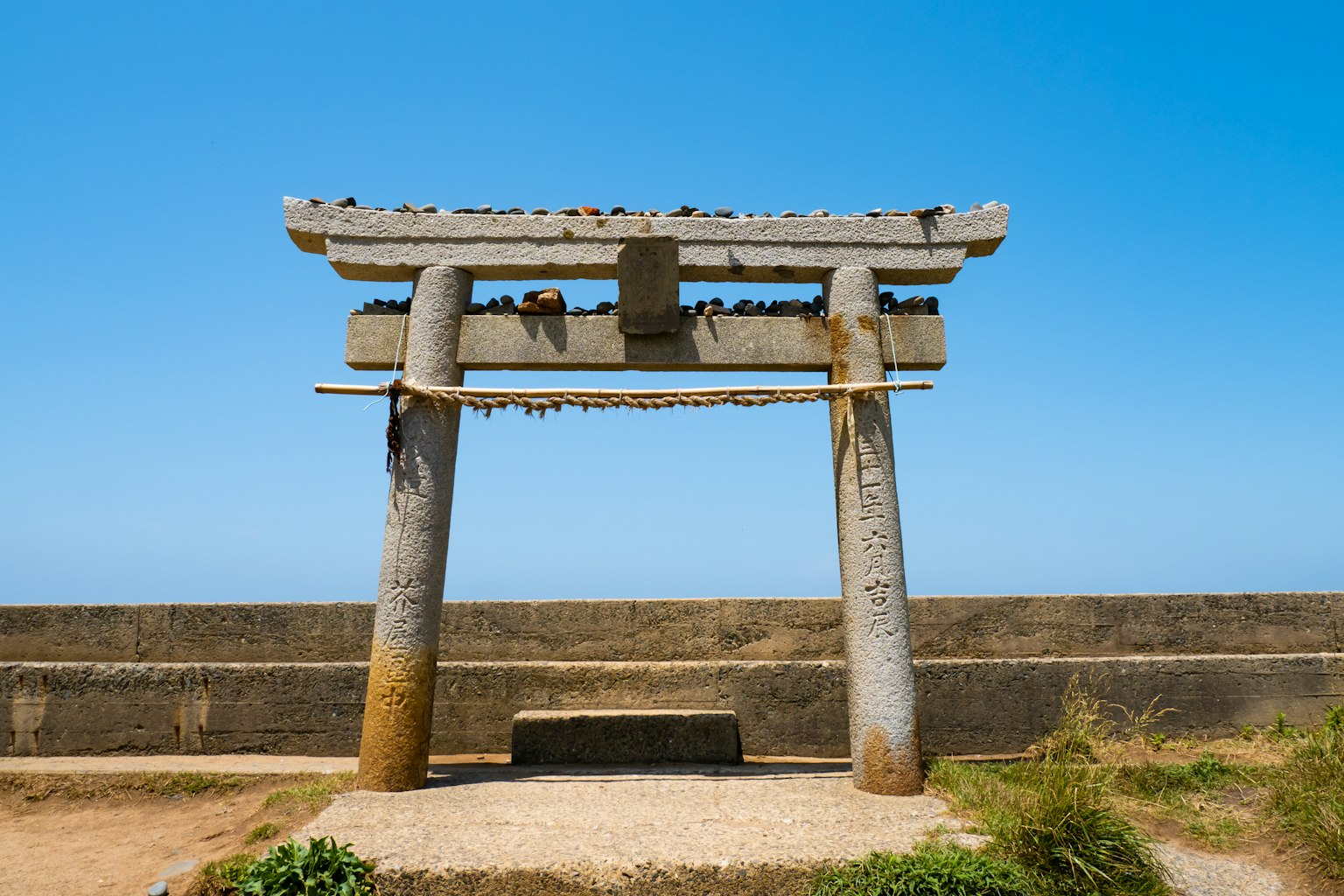 Antico torii e panchina in pietra sotto un cielo azzurro