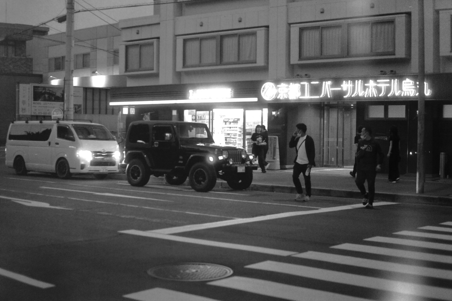 Black and white street scene featuring a Jeep and pedestrians