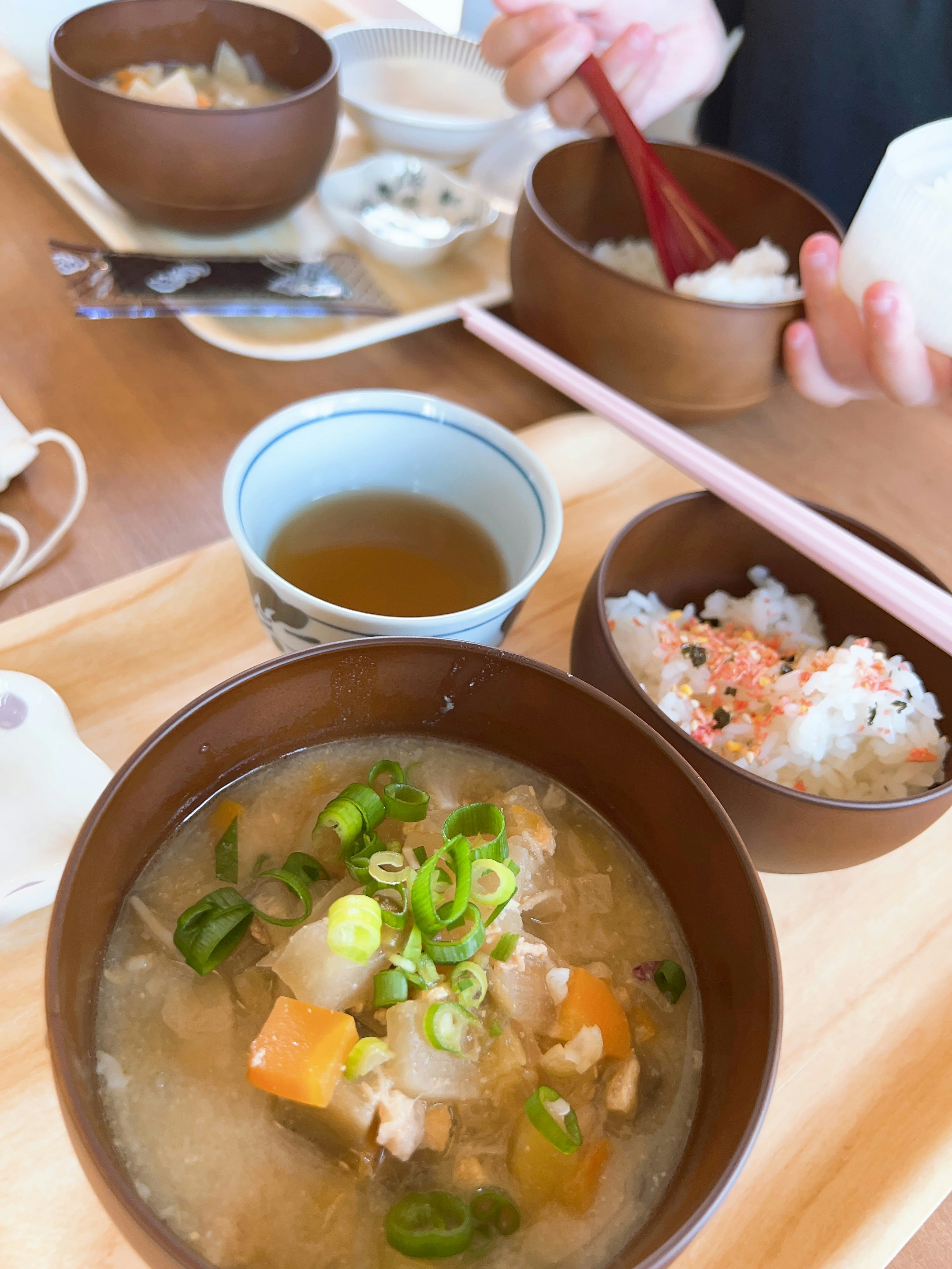 木のトレーに並ぶ和風の汁物と小鉢の食事