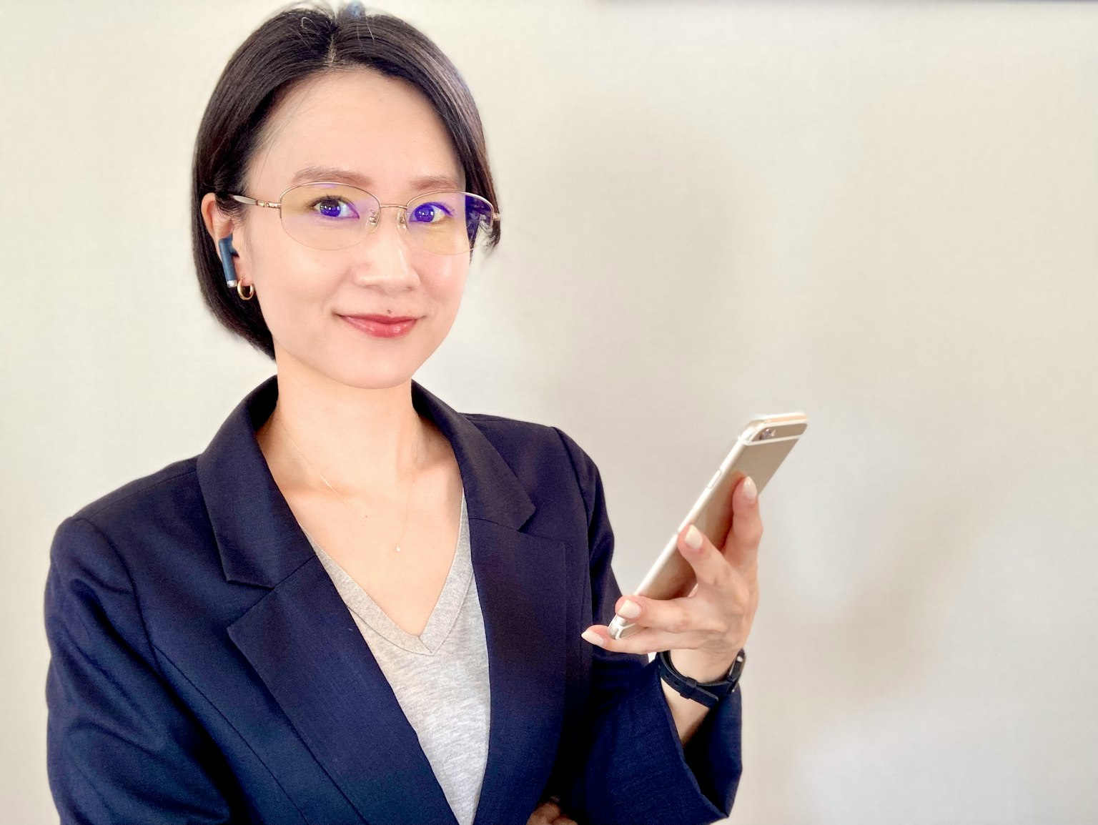 Seorang wanita berpakaian jas memegang smartphone dengan senyuman