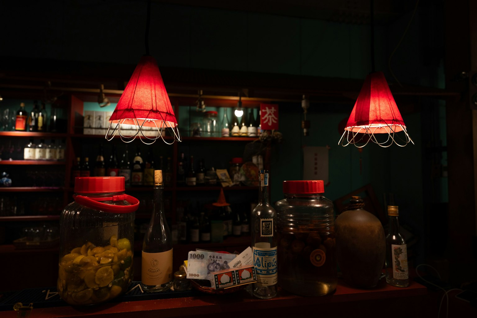 Comptoir de bar avec des abat-jours rouges et diverses bouteilles