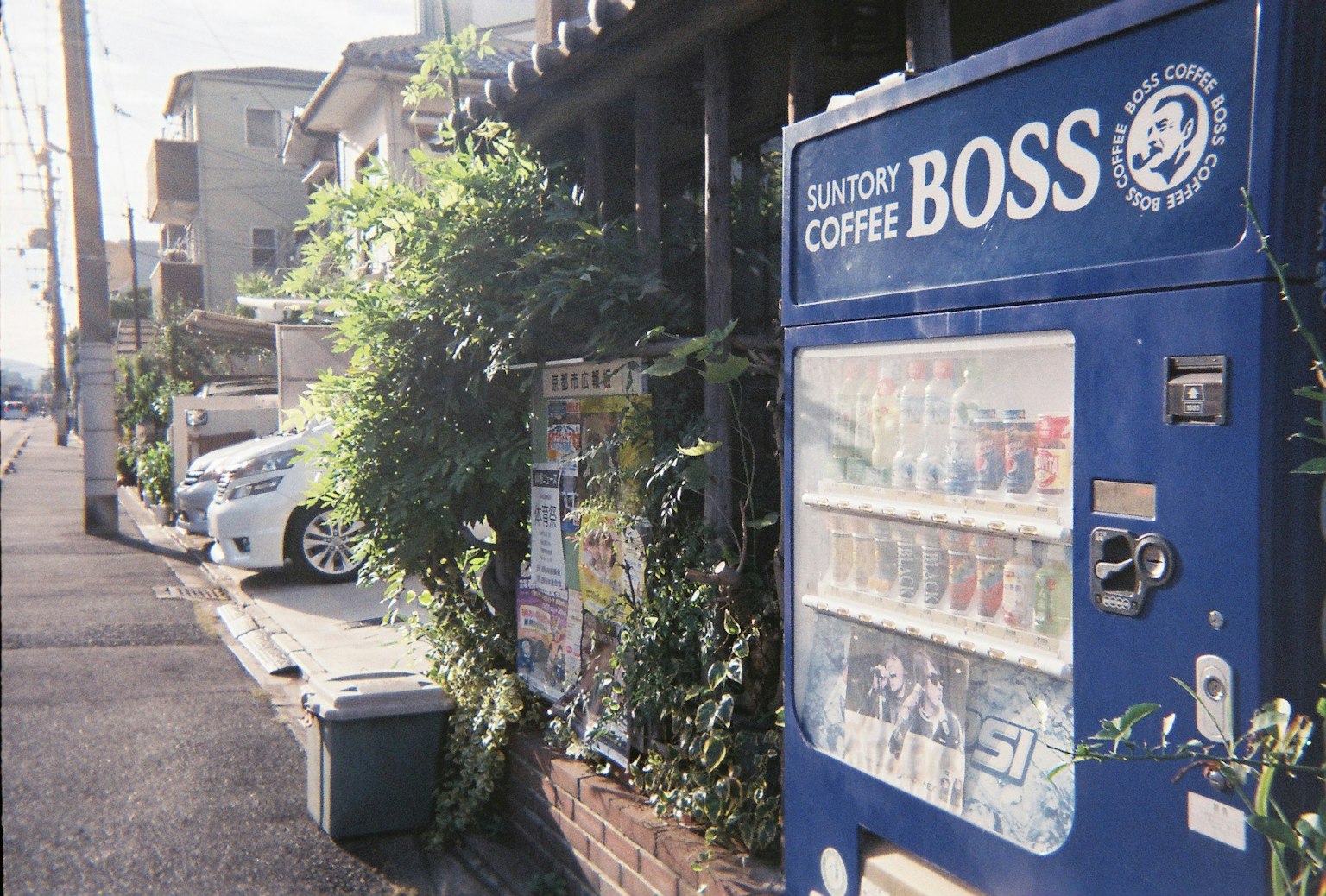 Street view featuring a blue vending machine surrounded by greenery